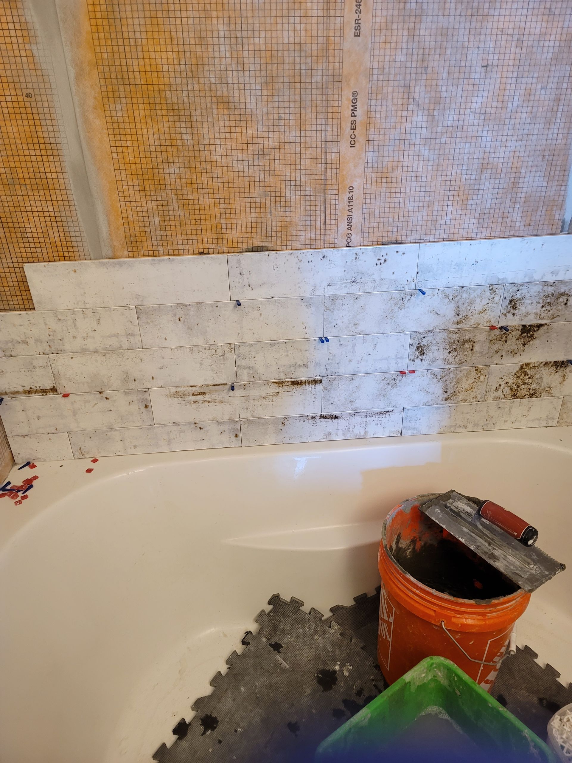 Bathtub wall with tile repair work, bucket, and trowel in a bathroom under renovation