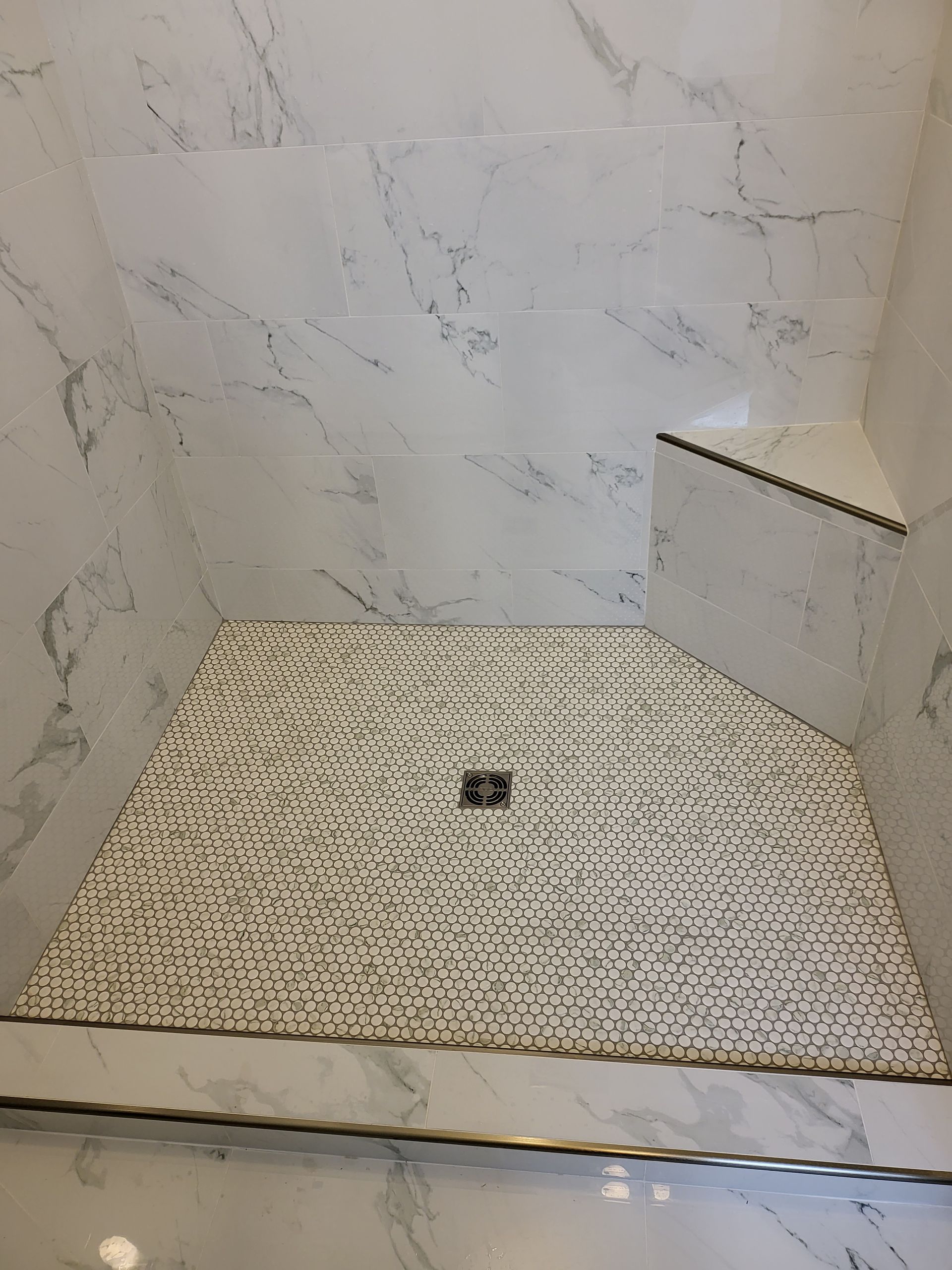 Empty tiled shower stall with built-in bench and shower drain.