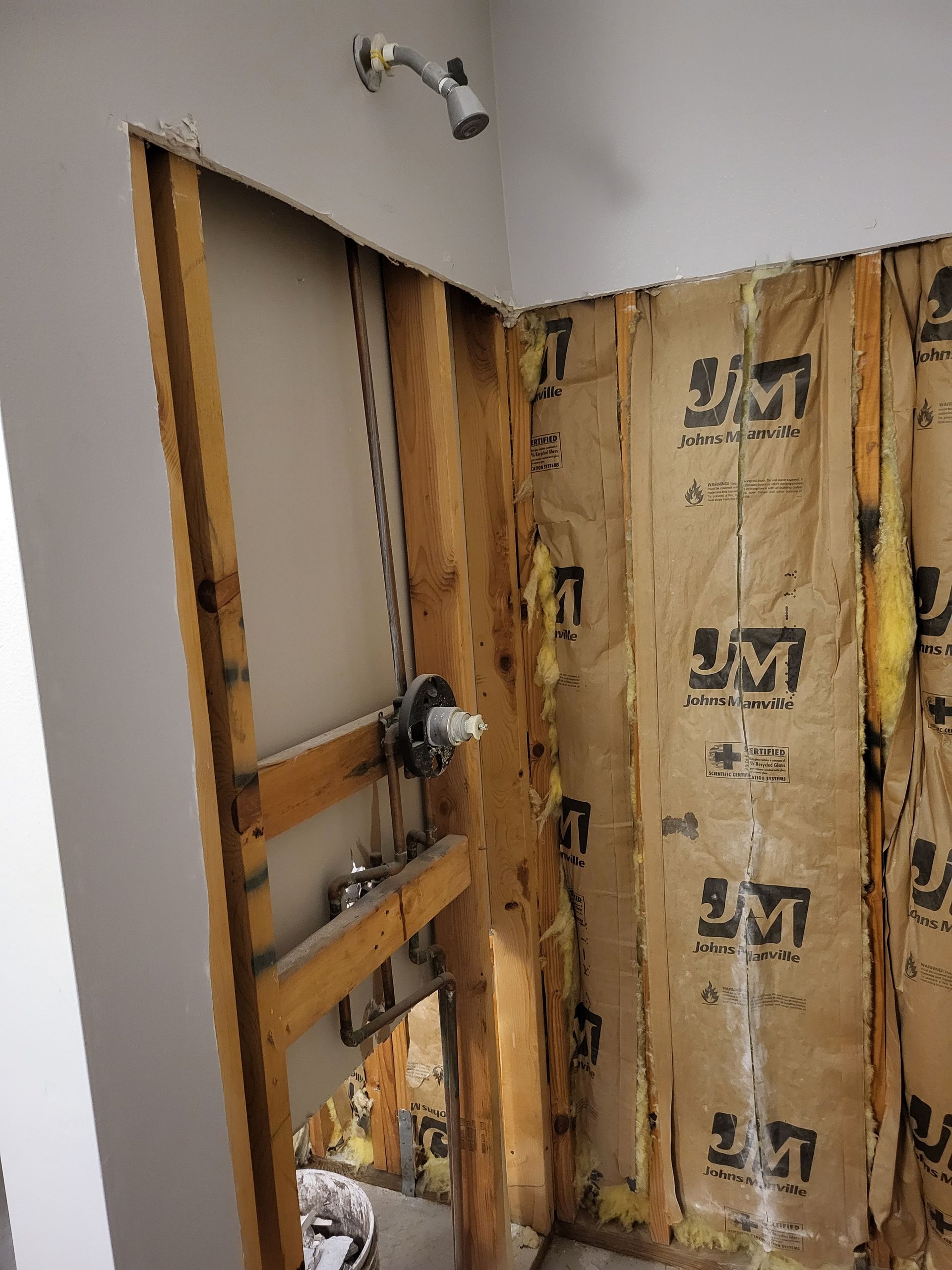 Interior wall under renovation with exposed studs, insulation, and plumbing near a doorway.