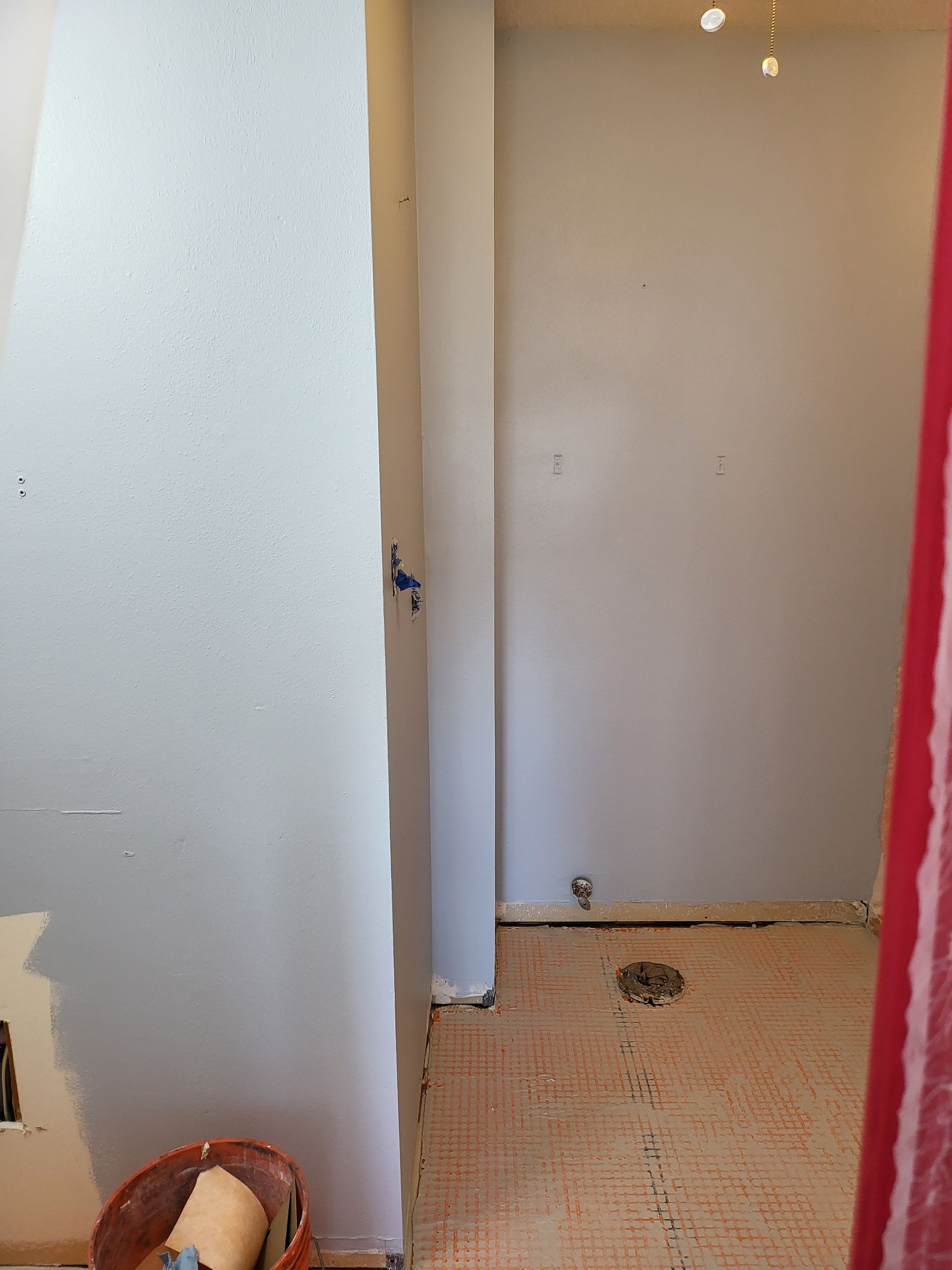 Partially renovated hallway with white walls, exposed floor, and a basket on the left.