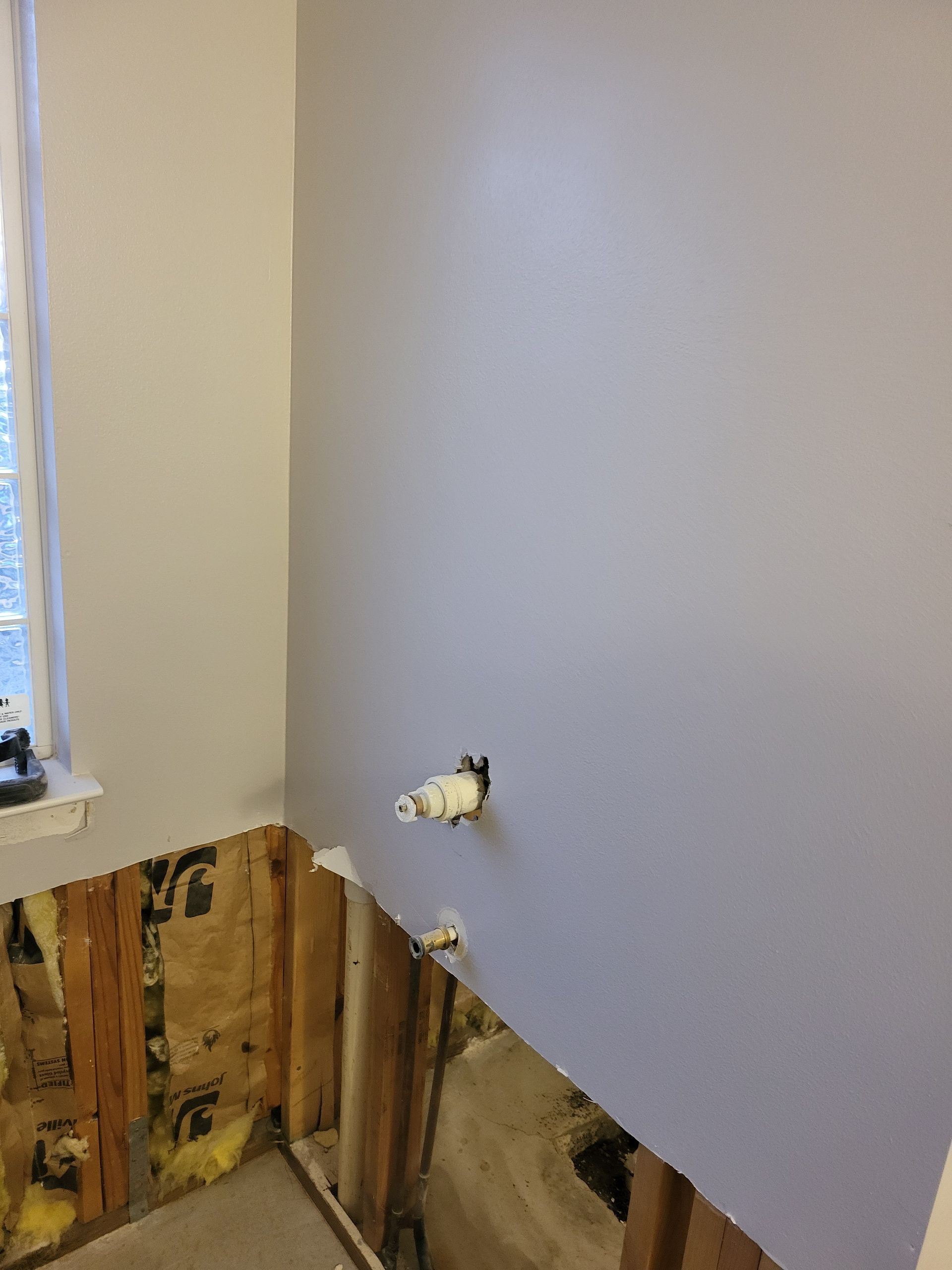 Partially stripped wall with exposed studs, electrical outlets, and a window in a room under renovation