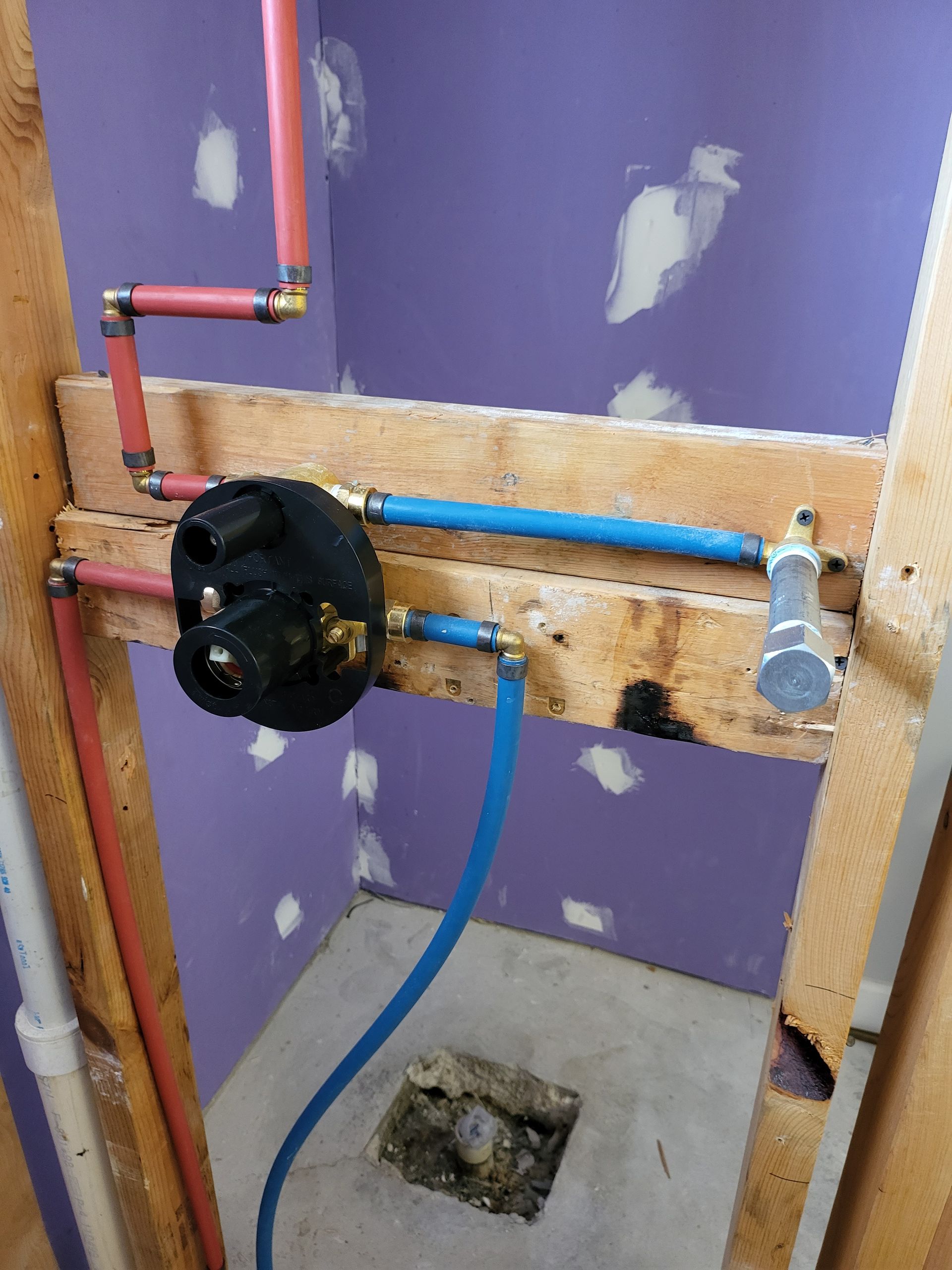 Partially built plumbing with pipes, valve, and drain in a purple-walled room