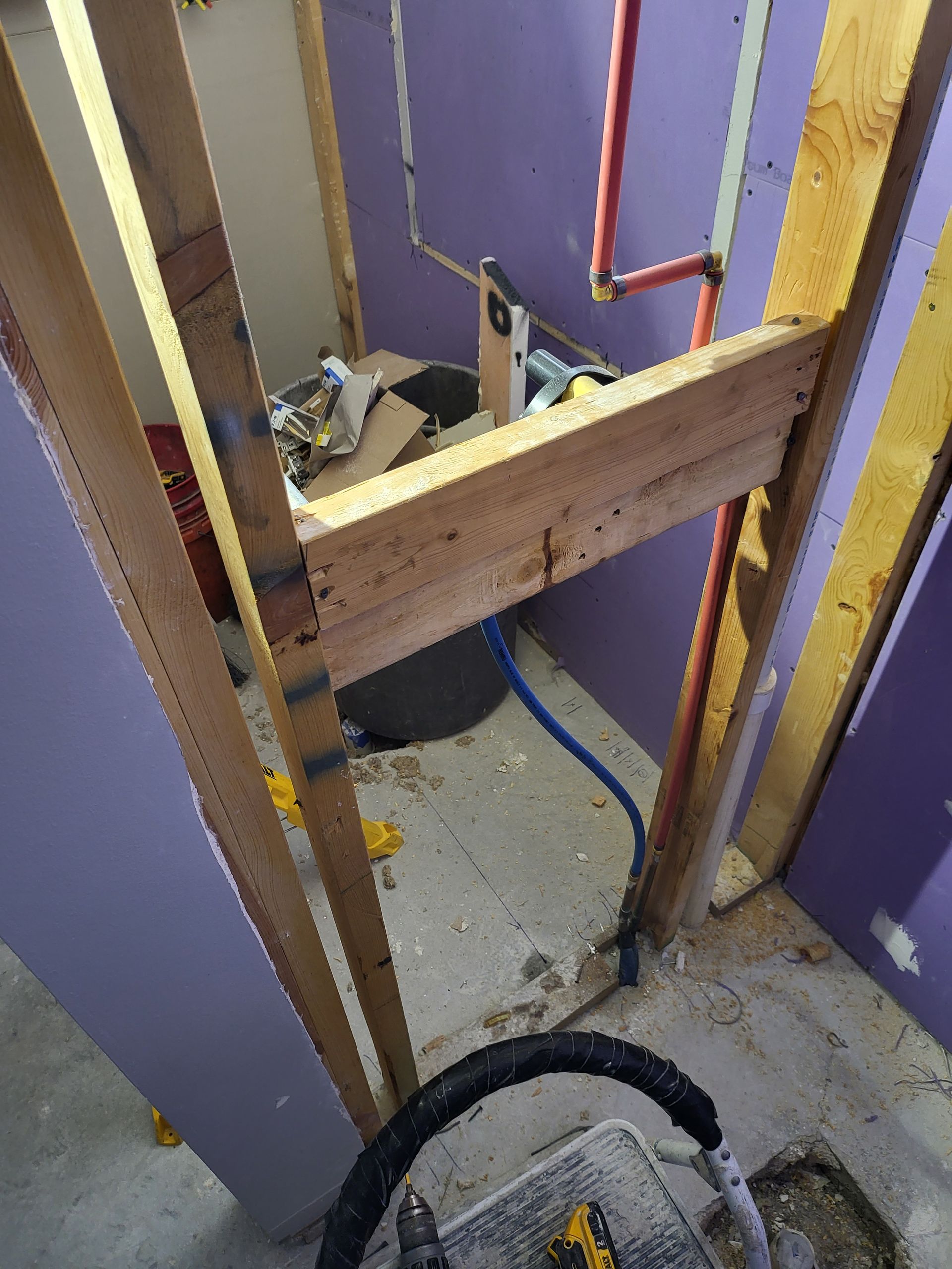 Partially framed shower nook with purple walls, exposed studs, and plumbing visible on a bathroom floor.