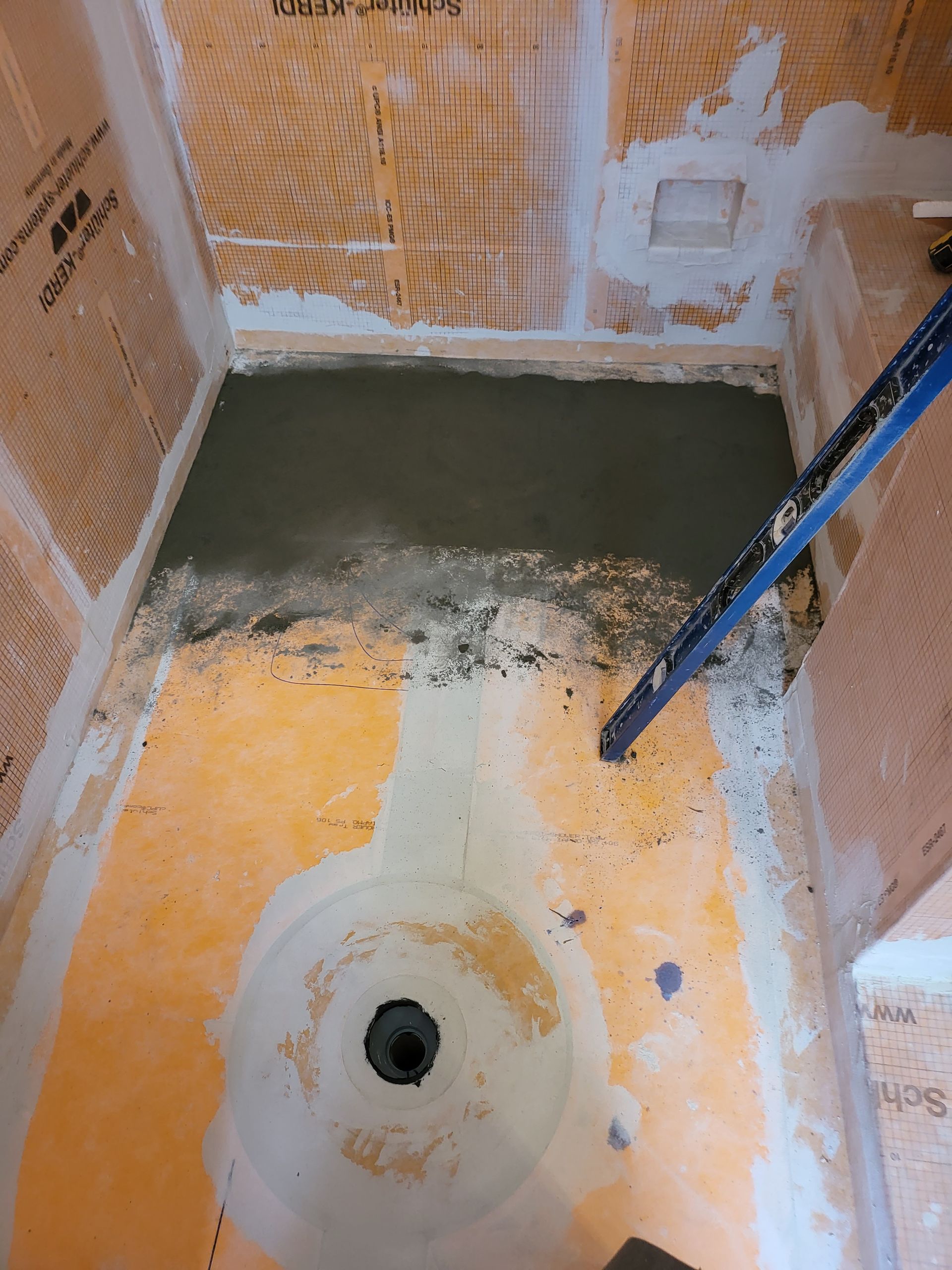 Partially finished shower floor with orange and gray waterproofing and a drain hole