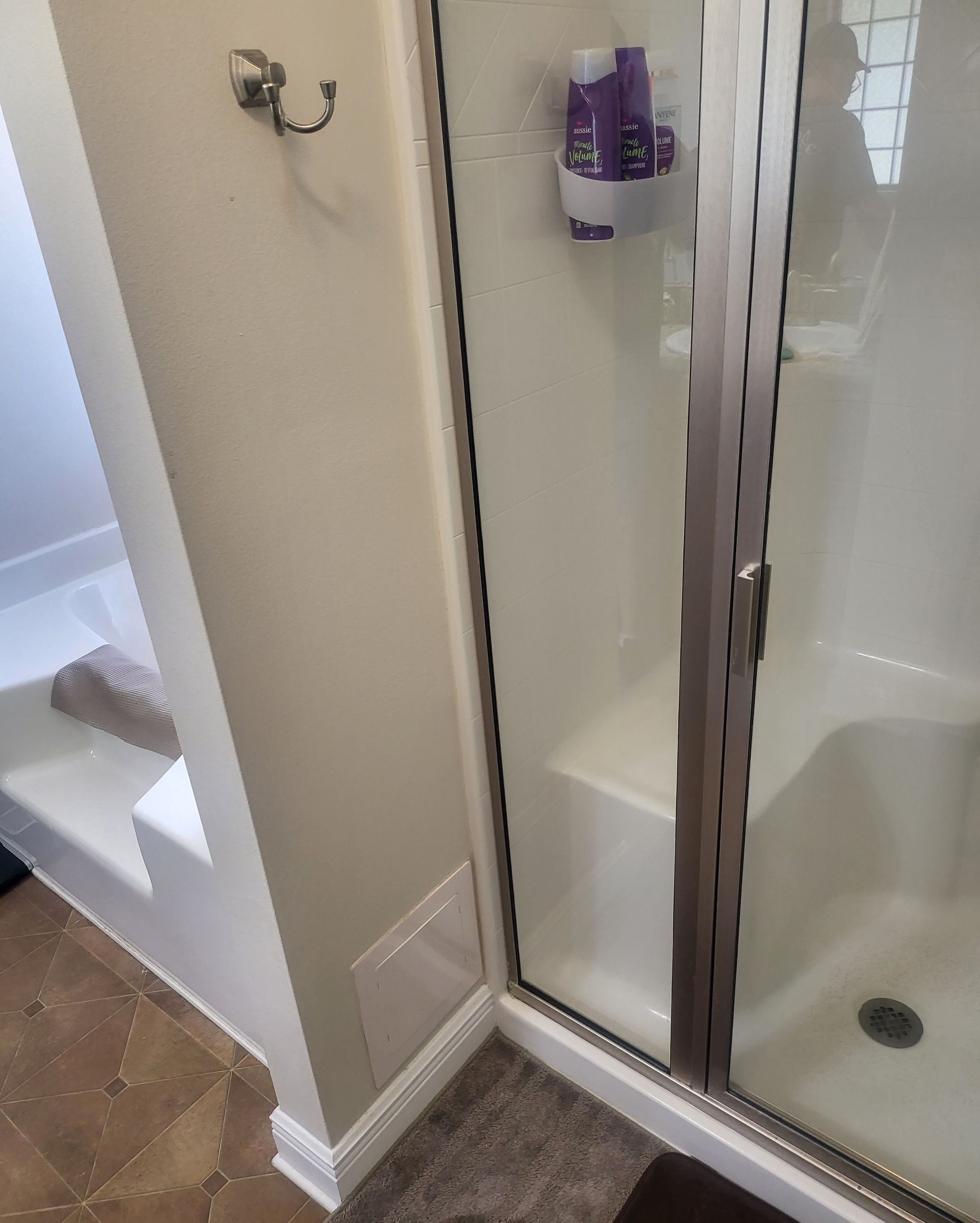 Shower stall with glass door, white walls, and wall-mounted purple soap dispenser beside tiled bathroom floor