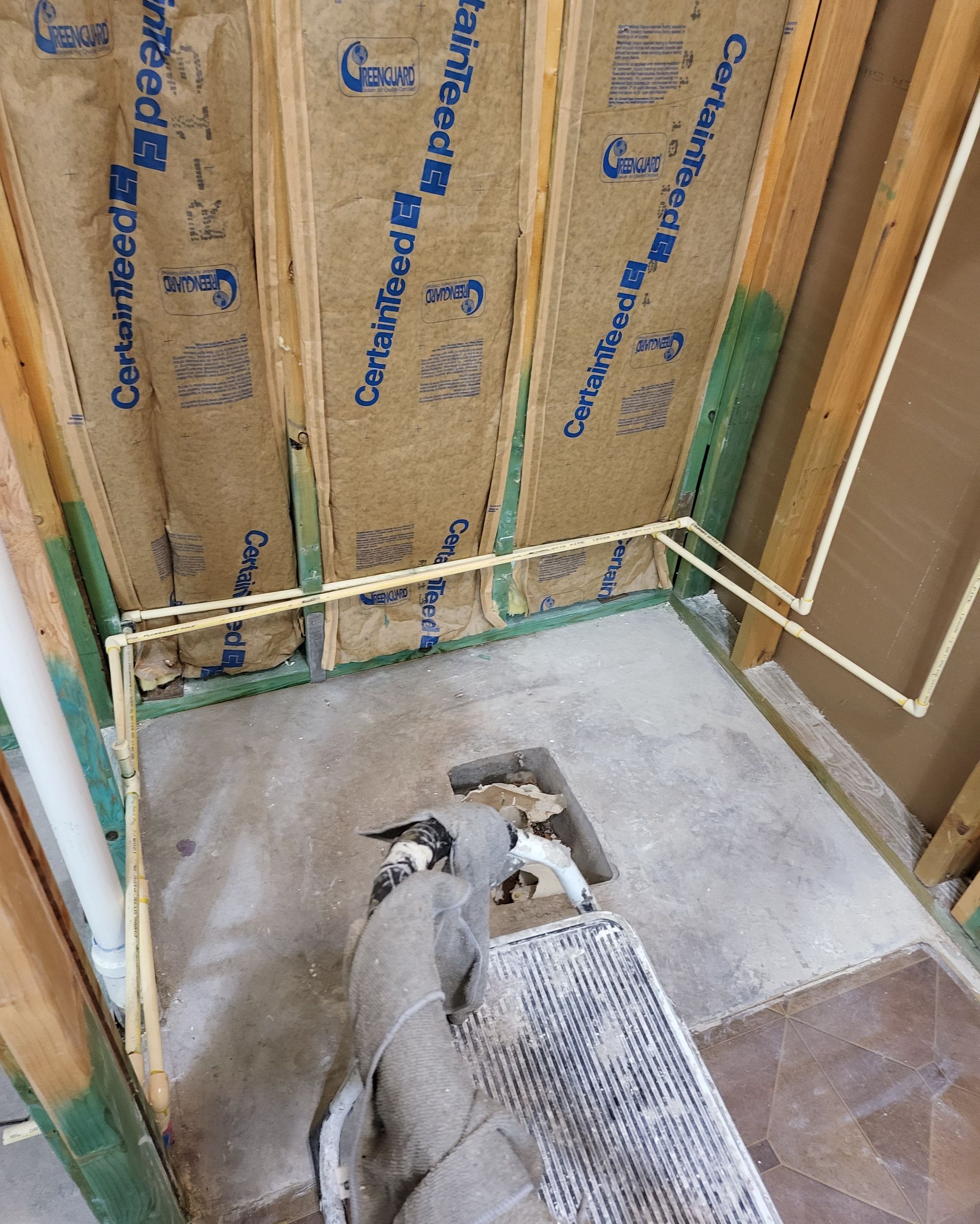 Exposed bathroom wall with insulation and plumbing rough-in above a concrete floor and drain.