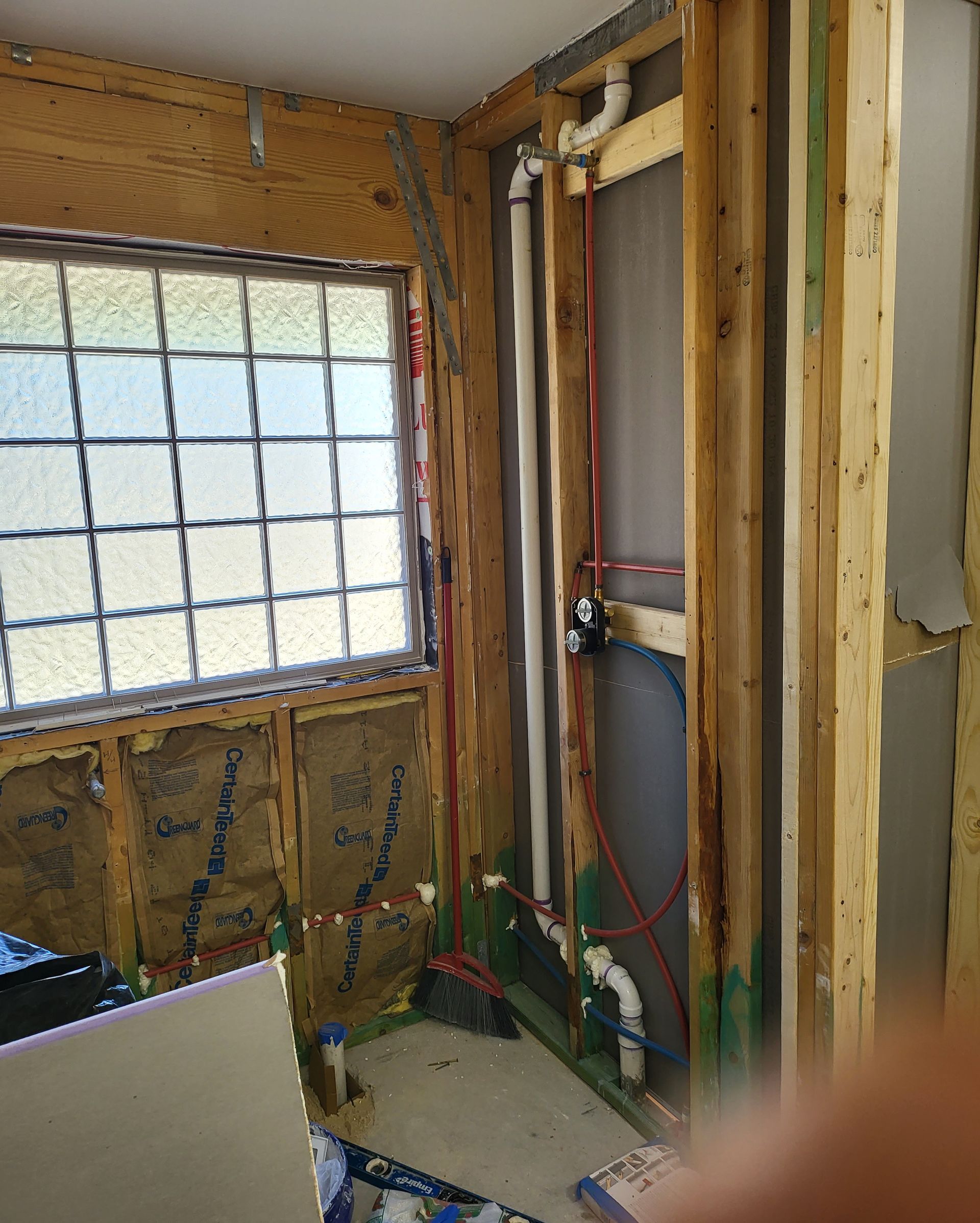 Framed wall under construction beside a window, with exposed wiring, insulation, and unfinished studs.