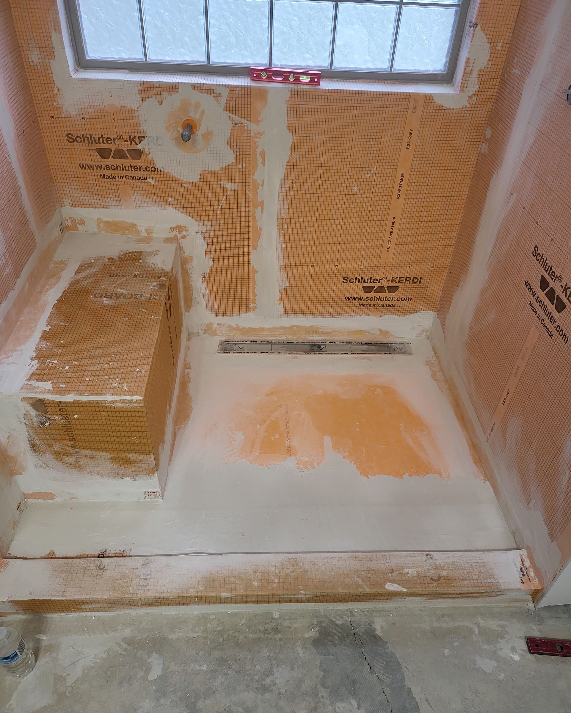 Partially plastered room with orange insulation panels, white floor patch, and a window above