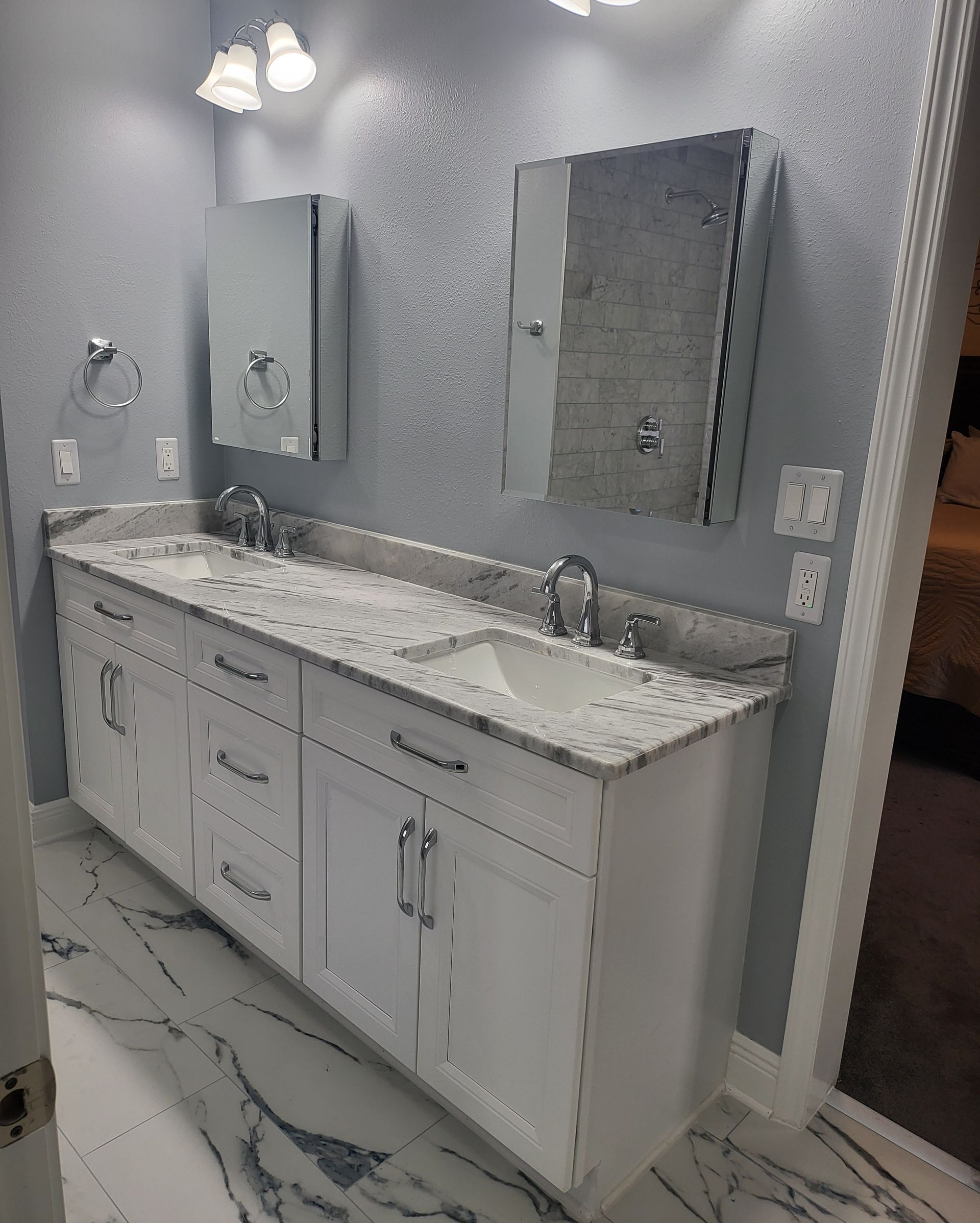 Modern bathroom vanity with double sinks, white cabinets, marble countertop, mirrors, and wall sconces.
