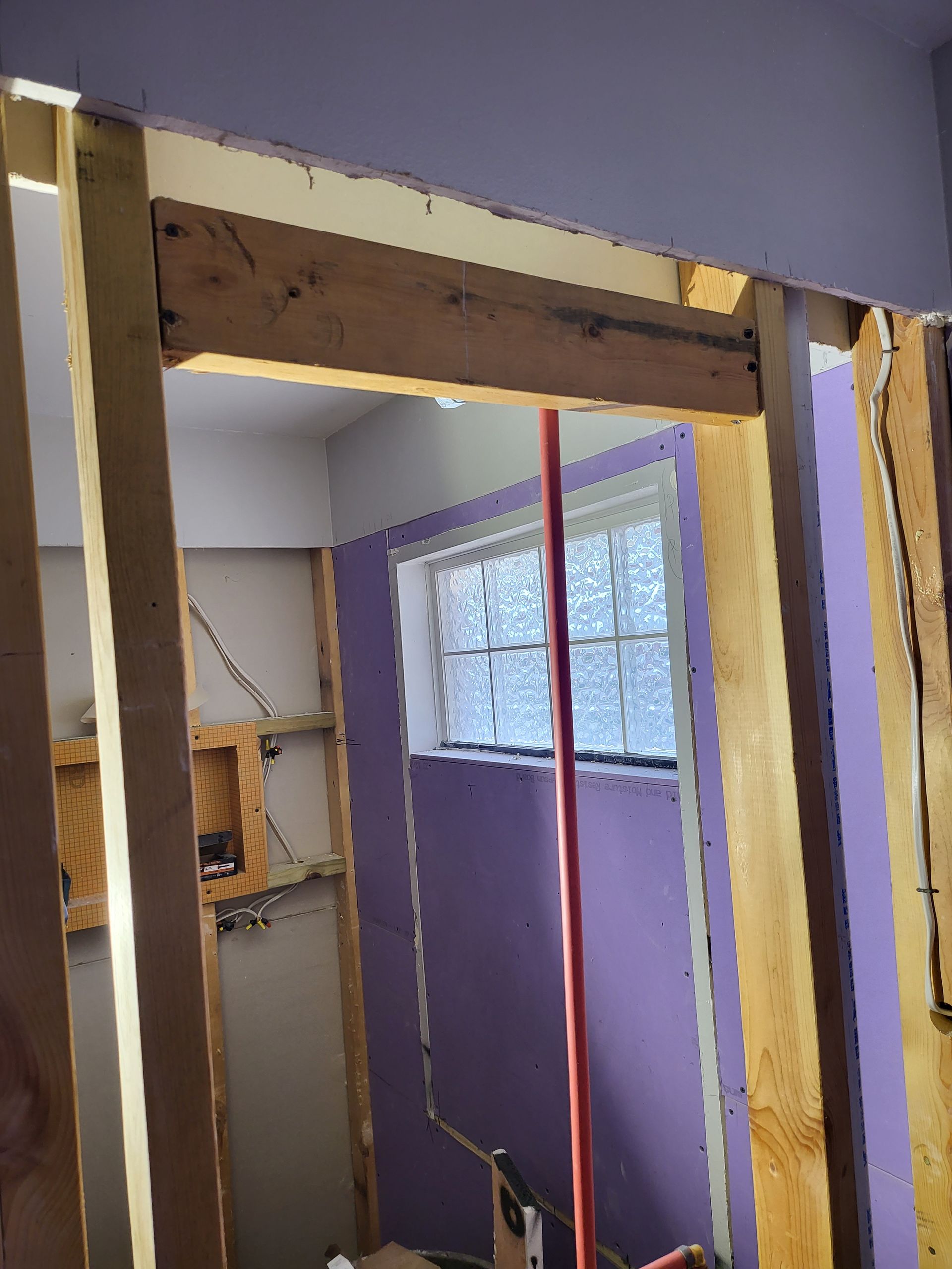 Interior renovation with exposed wooden framing around a doorway and a purple room visible beyond.