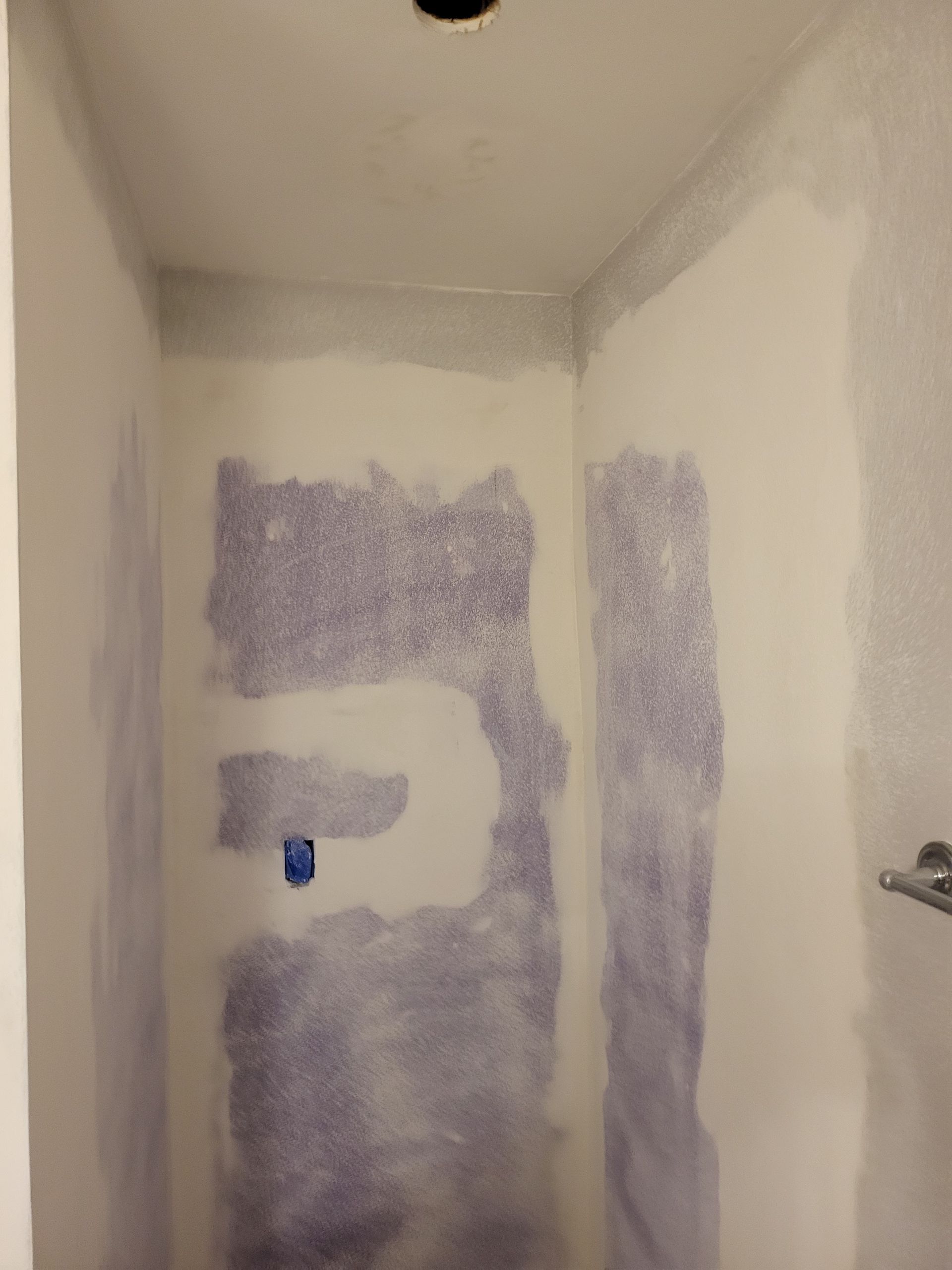 Bare drywall room with purple primer patches and a blue outlet box near the center wall