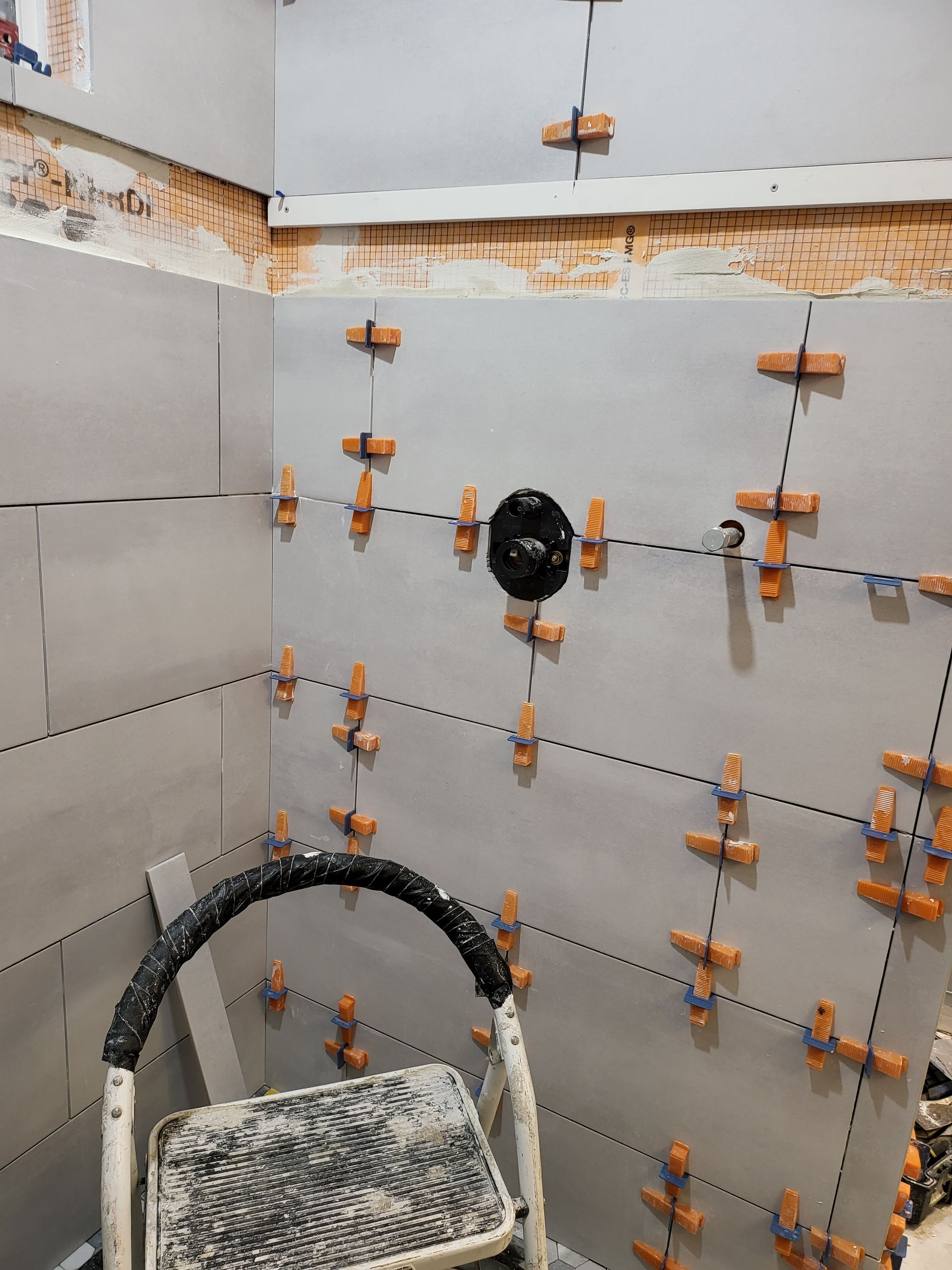 Partially tiled shower wall under construction with orange tile spacers and a black shower valve in the center