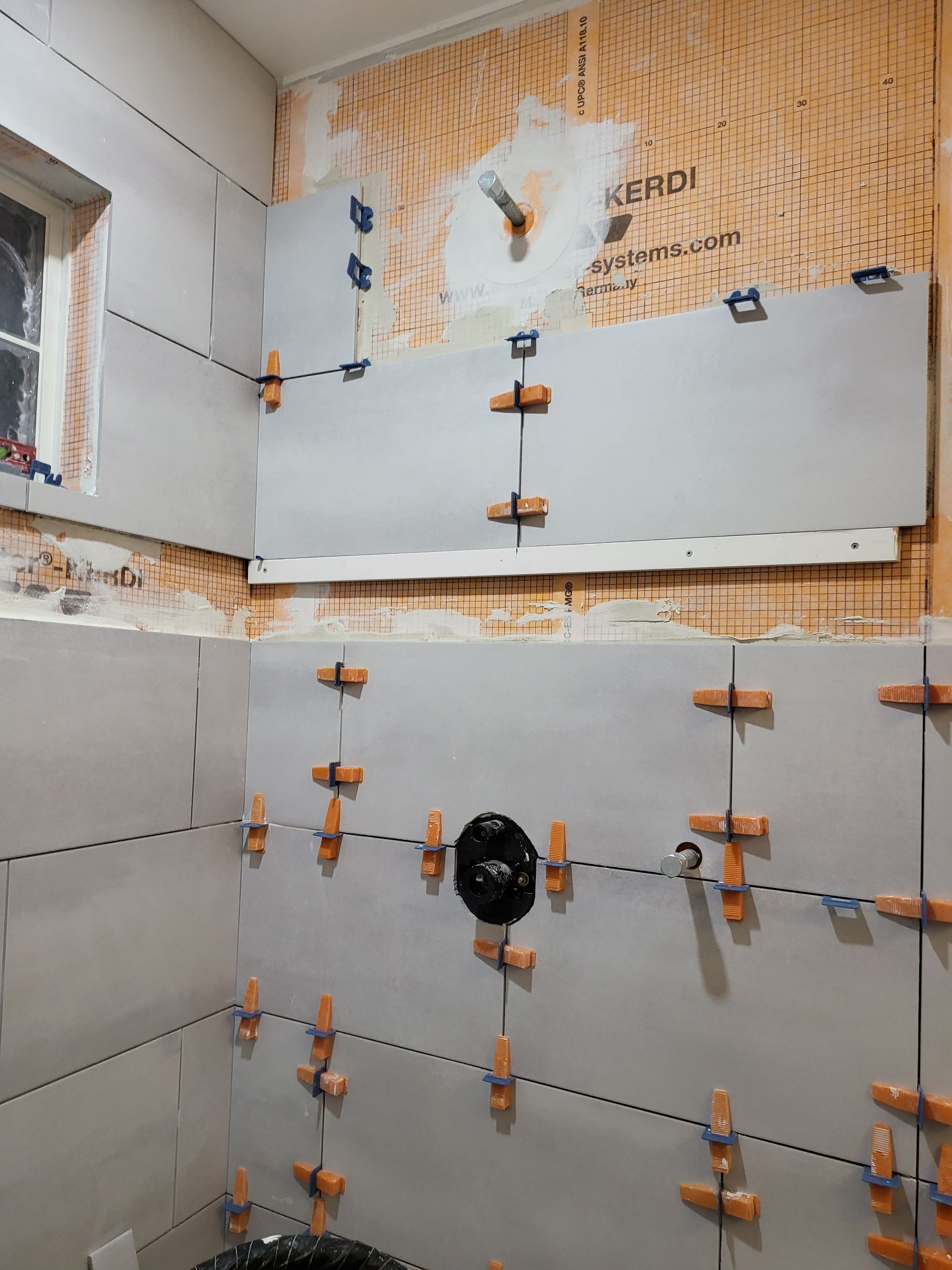 Bathroom under construction with gray wall panels, orange anchors, and exposed insulation.