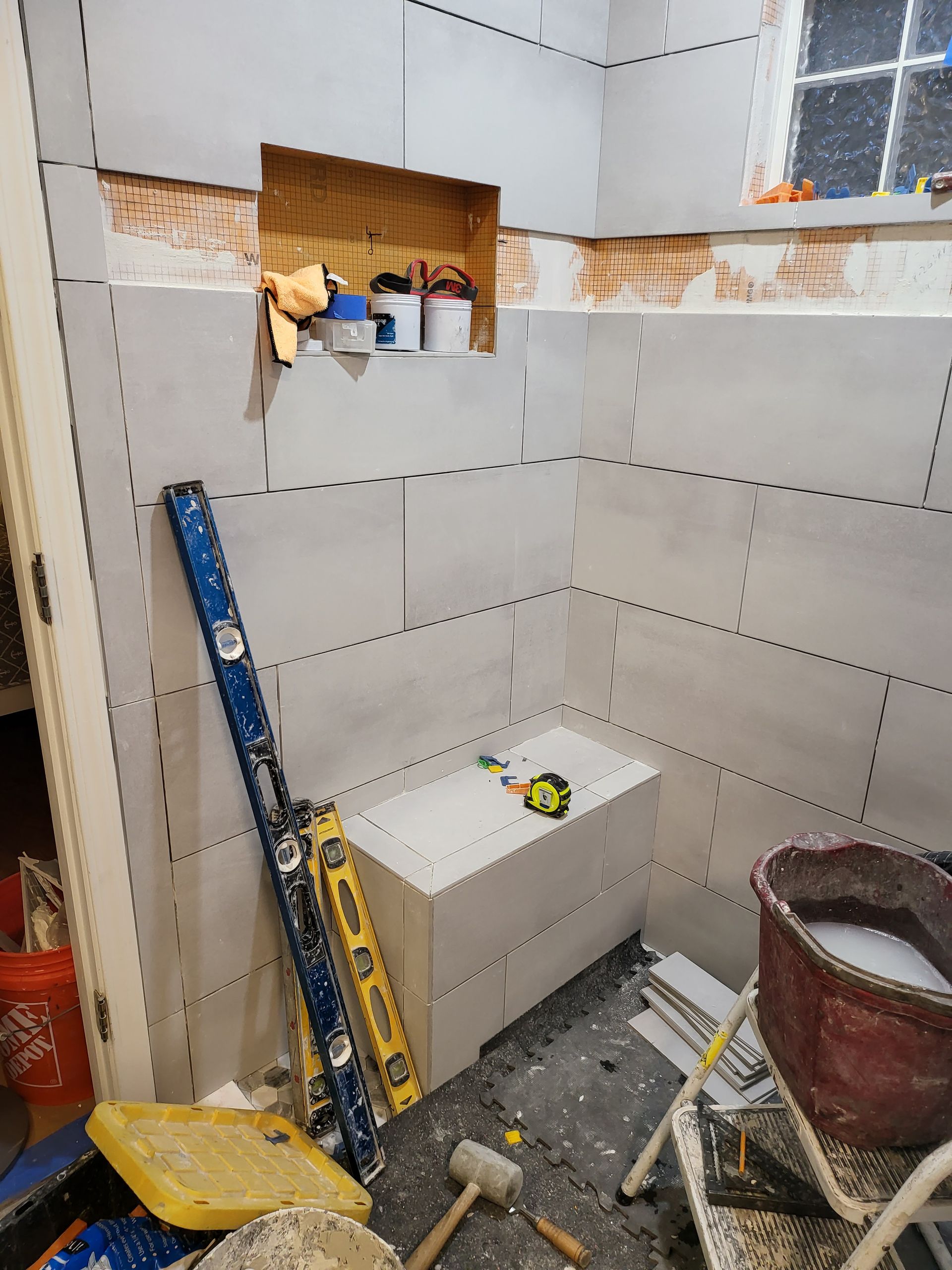 Partially tiled bathroom under renovation with tools, a bucket, and a toilet in place