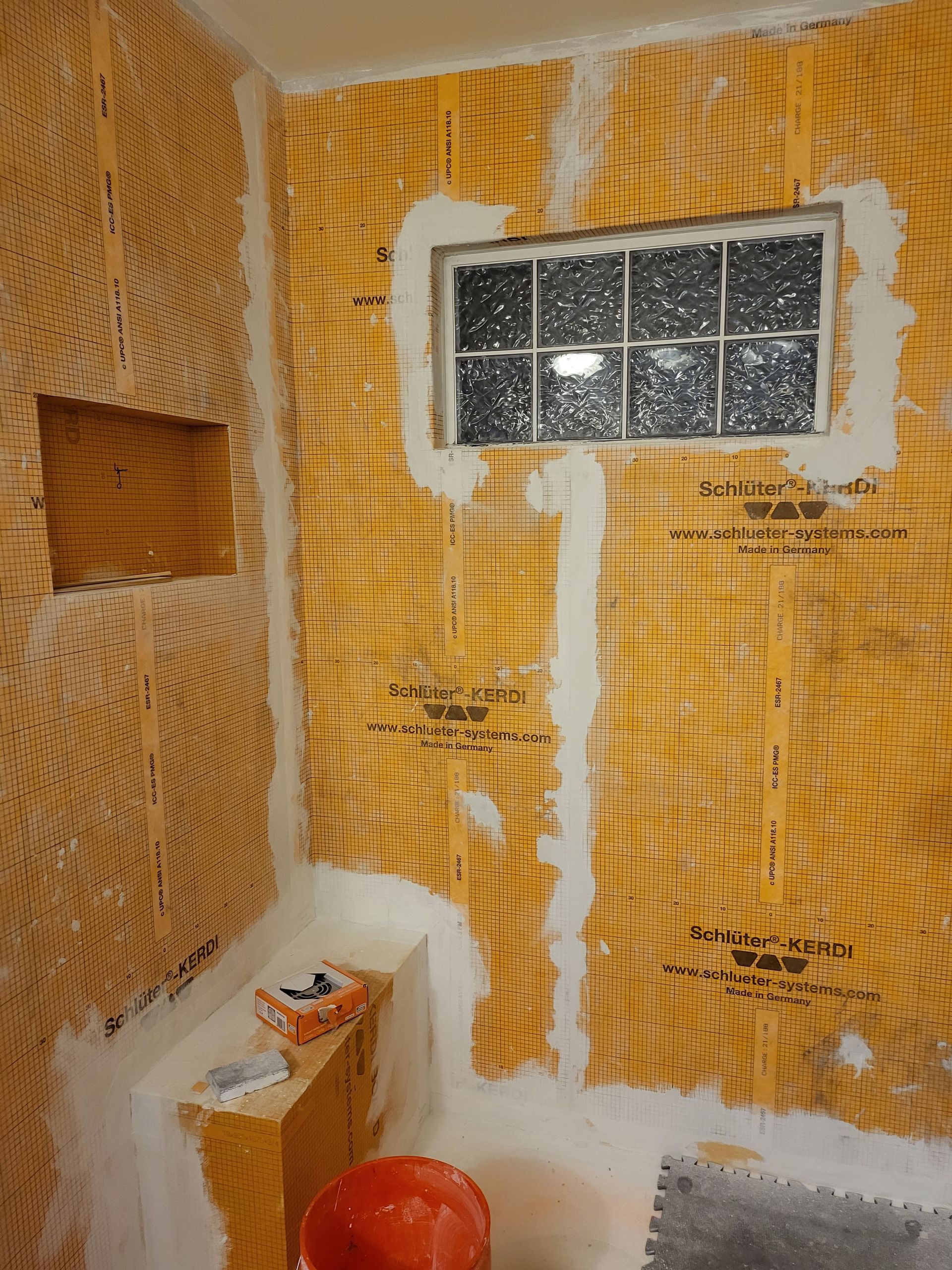 Bathroom under construction with insulation, exposed studs, window, and a red bucket on the floor