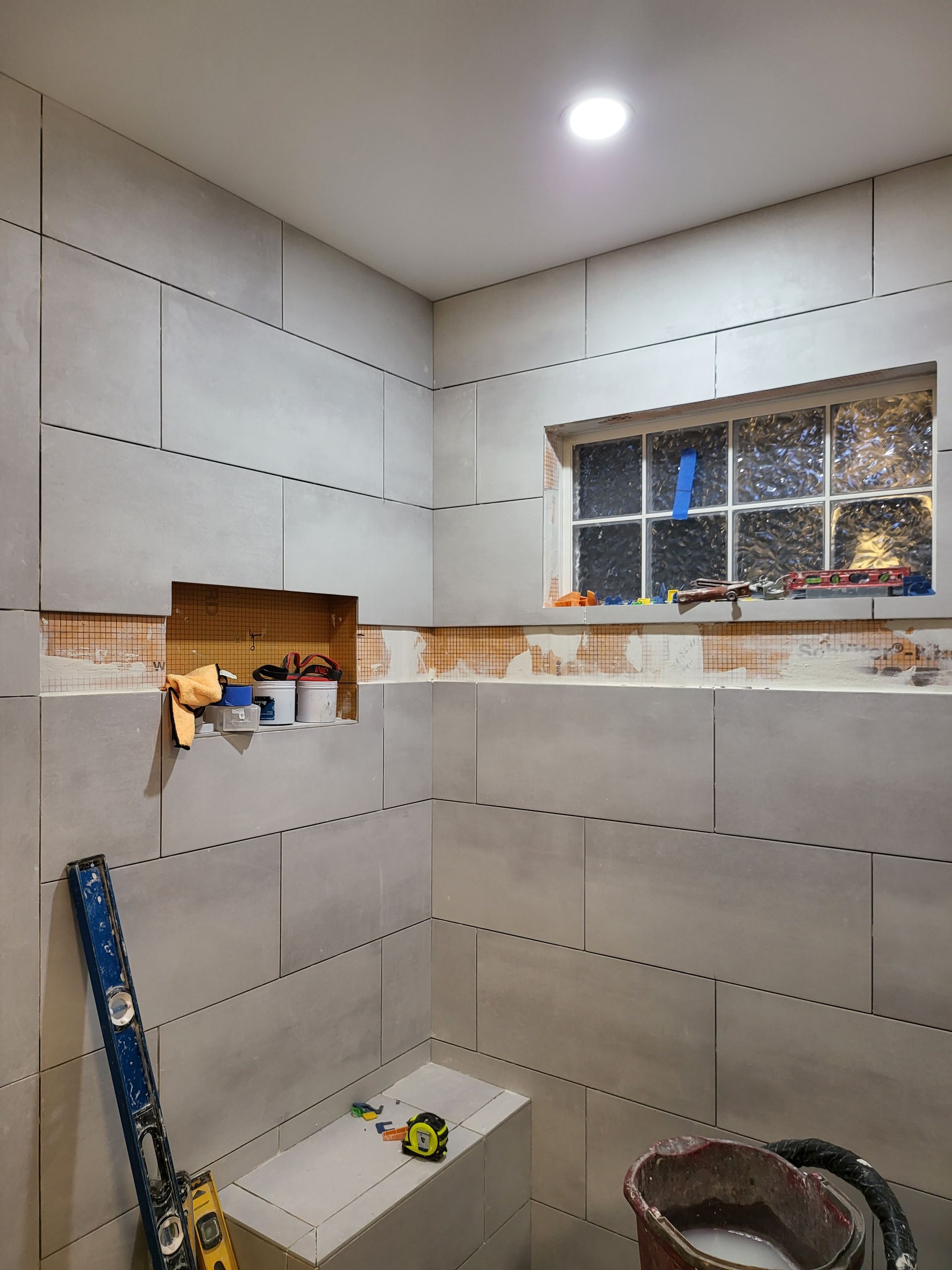 Bathroom under construction with tiled walls, a recessed wall opening, and a window.