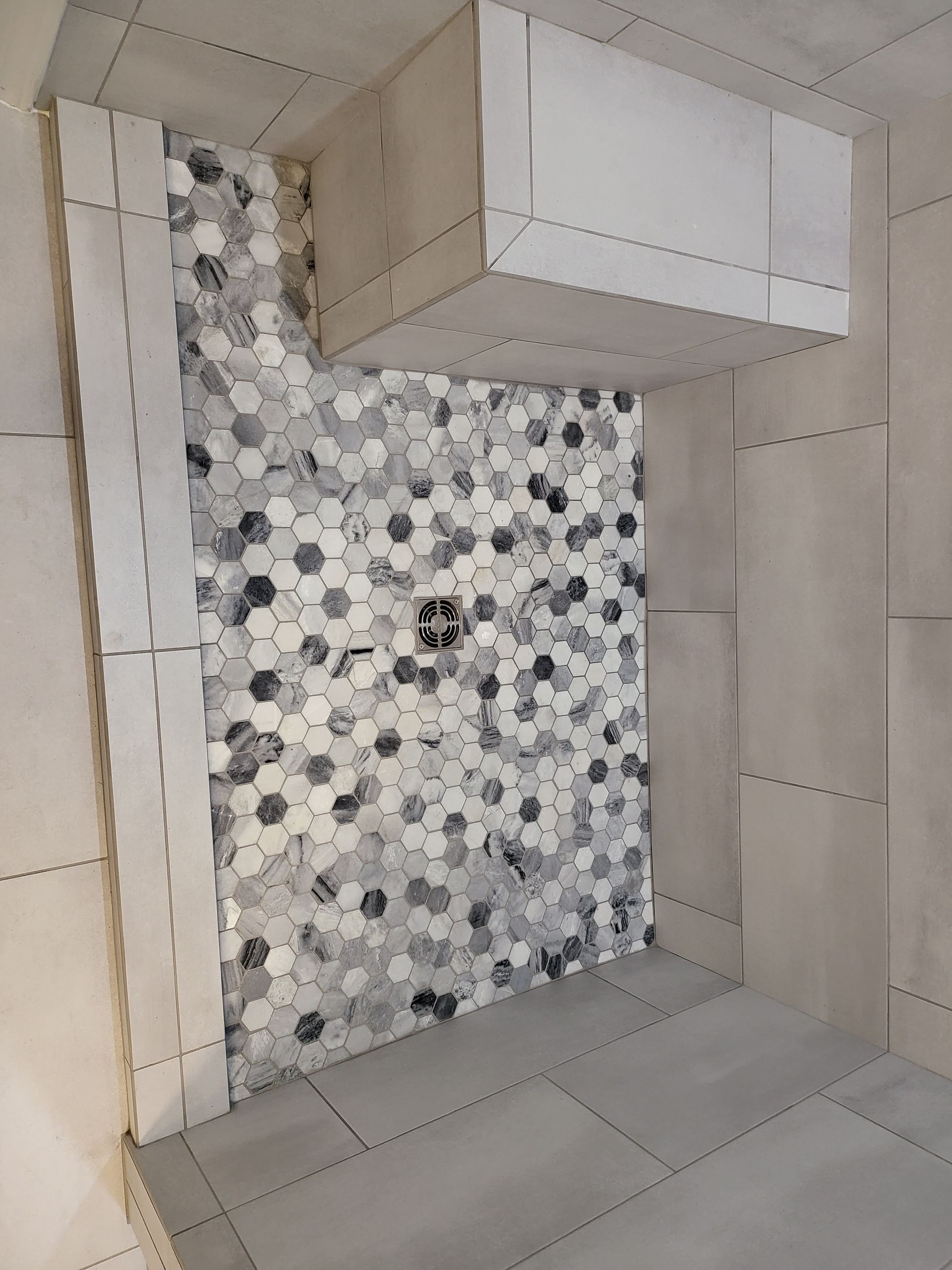 Small tiled bathroom shower with gray floor tiles and a white vanity cabinet above a mosaic accent wall.