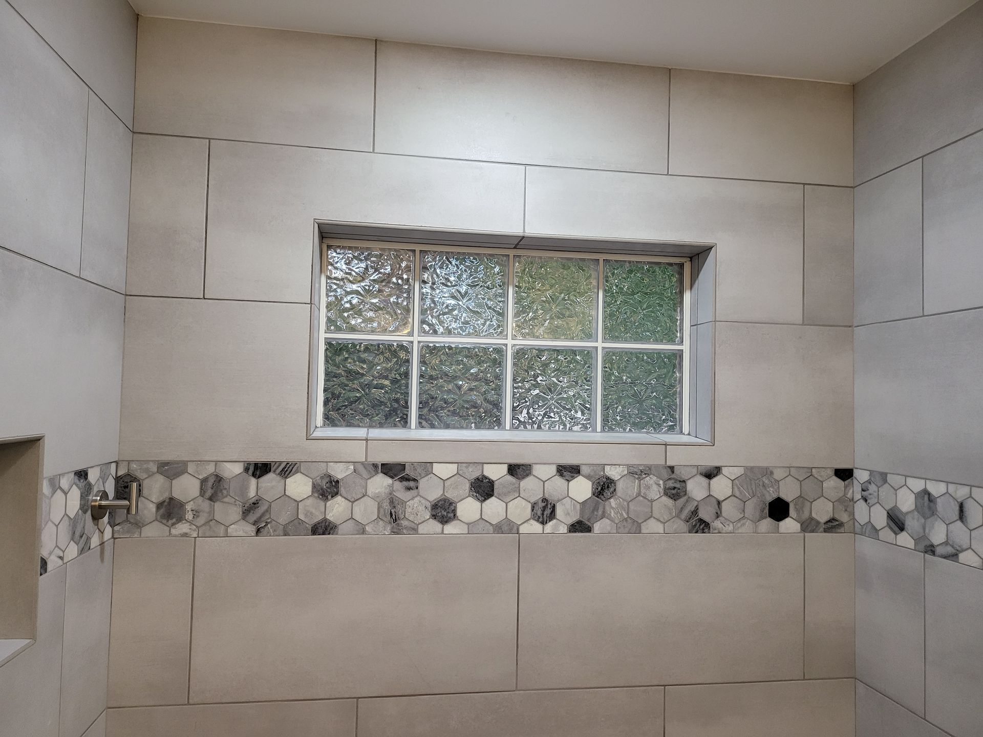 Tiled bathroom wall with a small window and decorative mosaic accent strip.