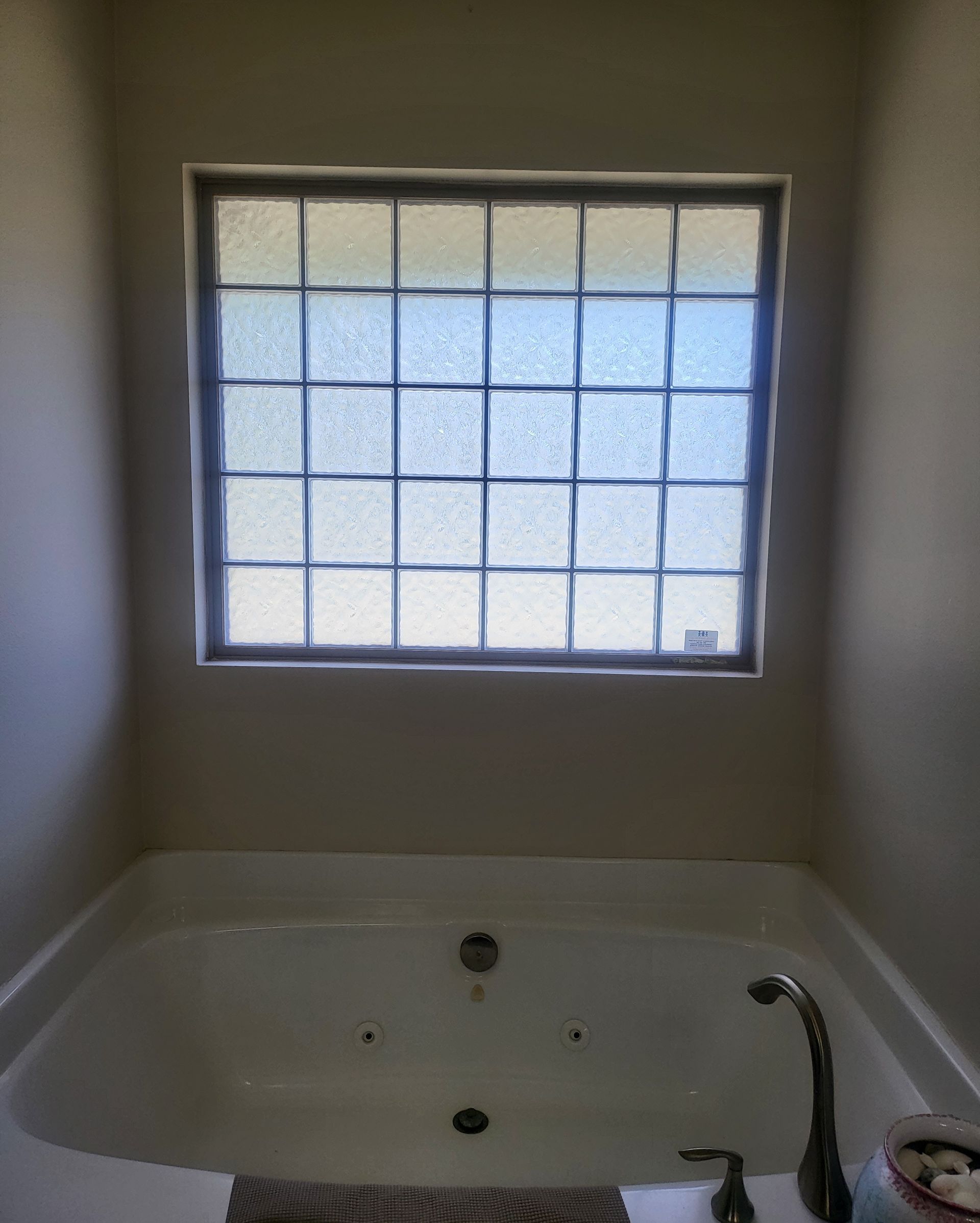 Bathtub beneath a frosted window in a small bathroom, with a faucet and shower wand.