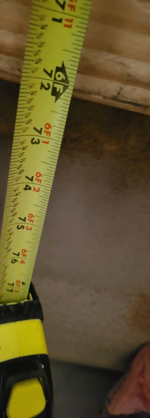 Yellow tape measure stretched vertically against a wooden surface, showing inch markings.