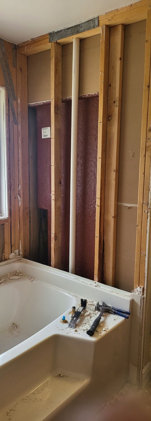 Bathroom with exposed wall studs behind a white tub and shower fixtures, under renovation