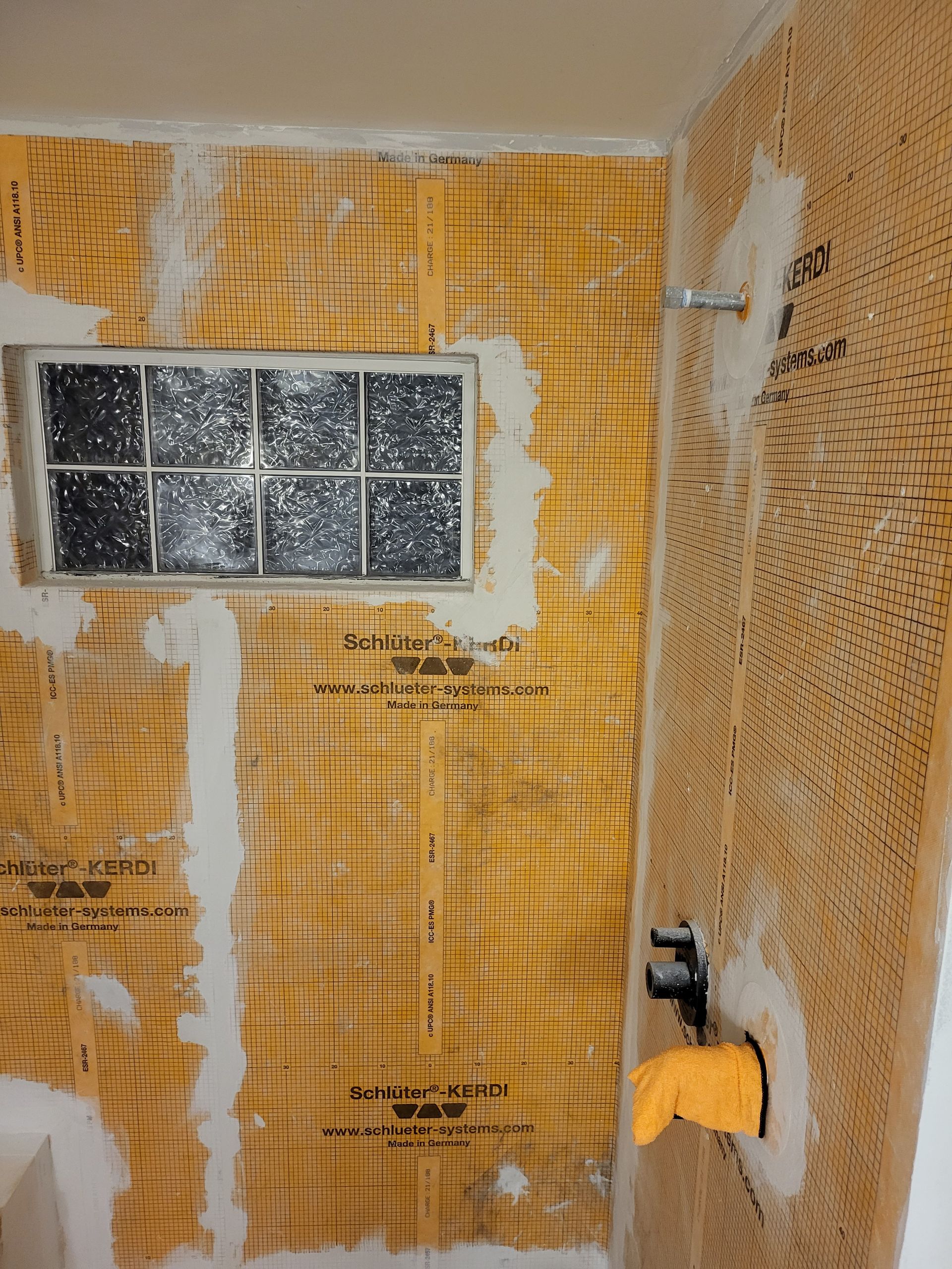 Partially tiled bathroom wall with a small frosted window and exposed yellow waterproofing grid