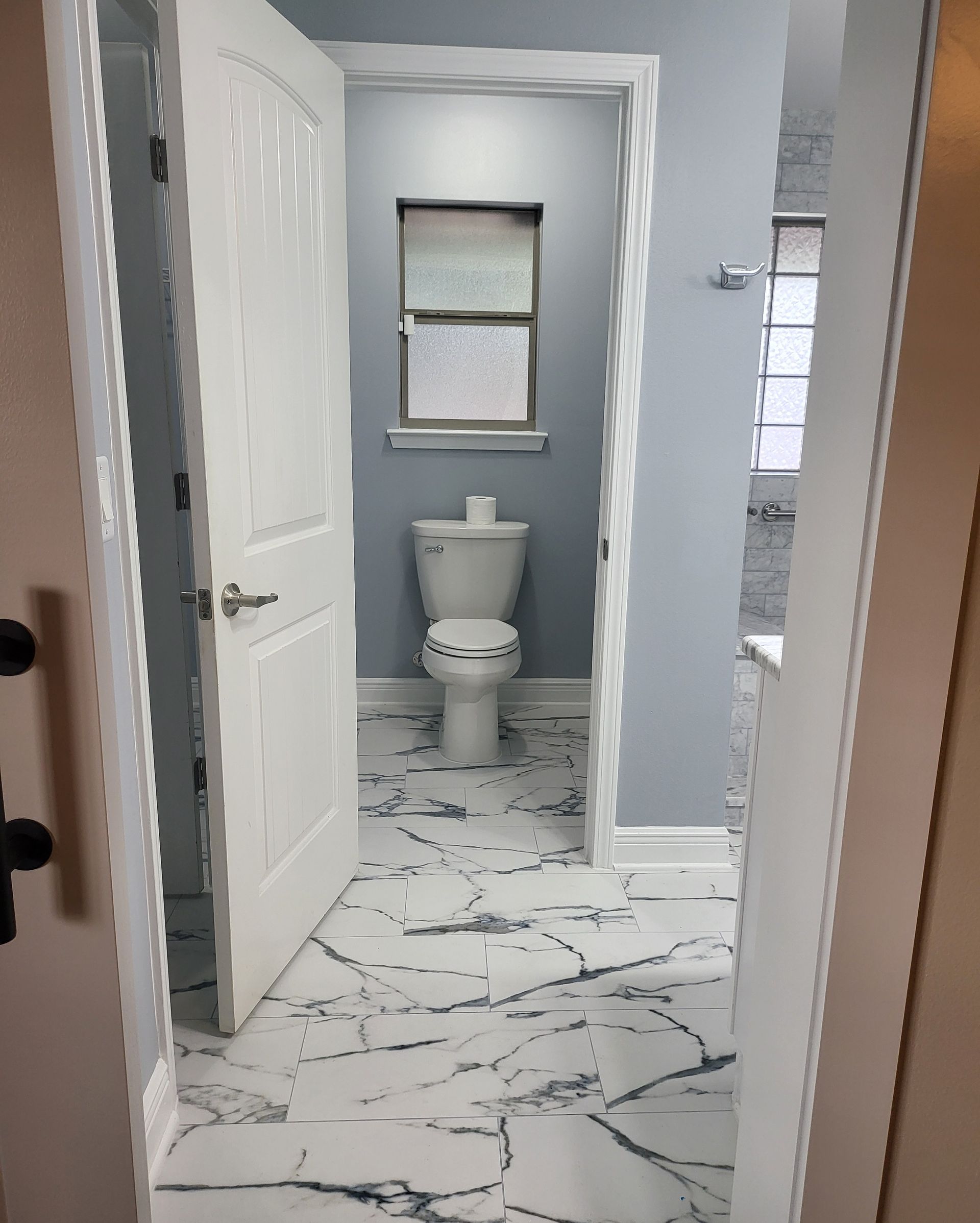 Small bathroom with gray walls, white toilet, and white marble-pattern tile floor viewed through an open doorway.