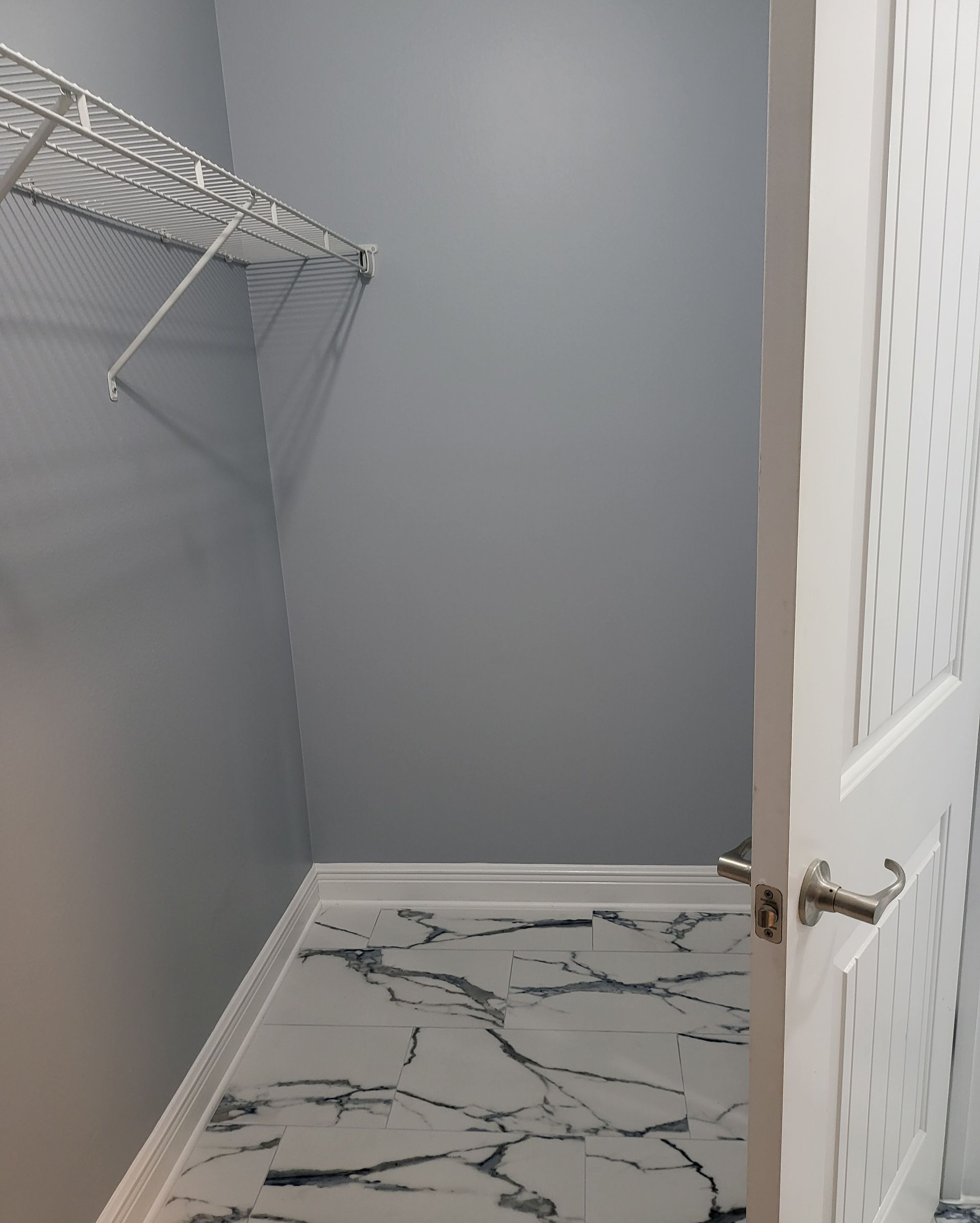 Empty gray walk-in closet with wire shelving, white doors, and patterned rug flooring.