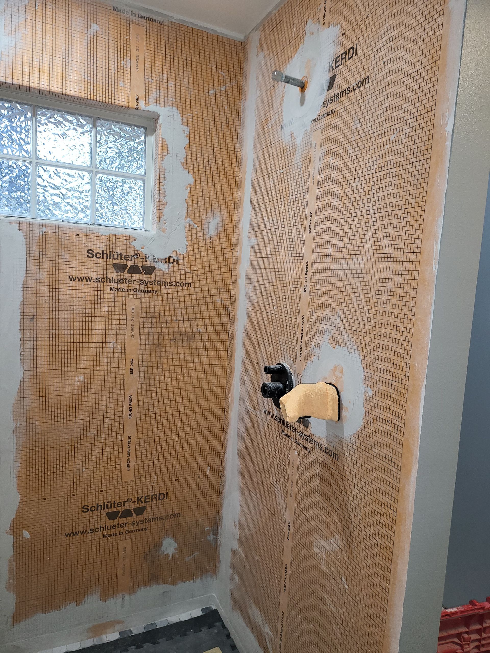 Bathroom wall with torn wallpaper, a small window, and exposed plumbing fixtures under renovation