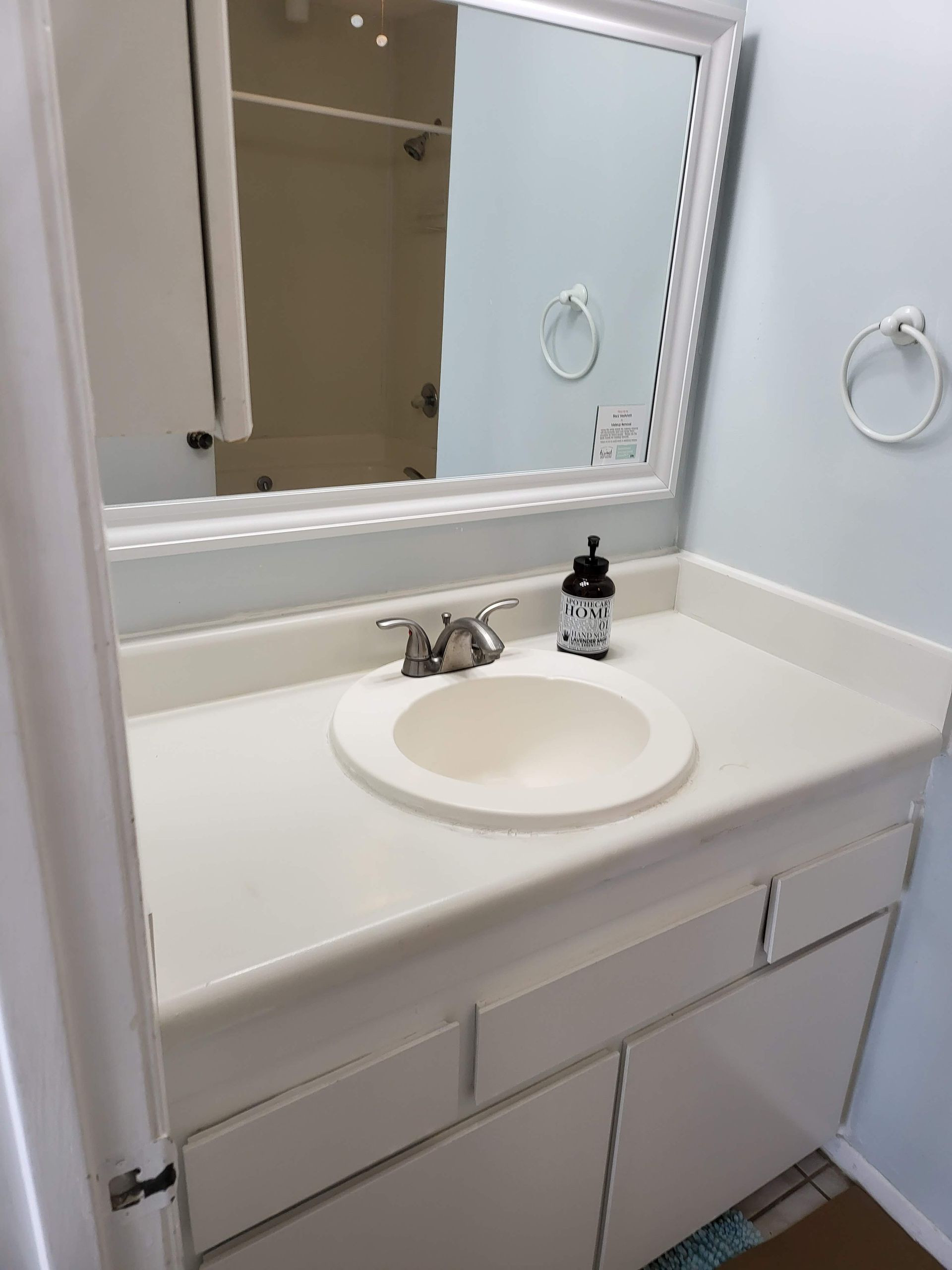 White bathroom vanity with round sink, mirror, faucet, and soap dispenser next to a shower doorway