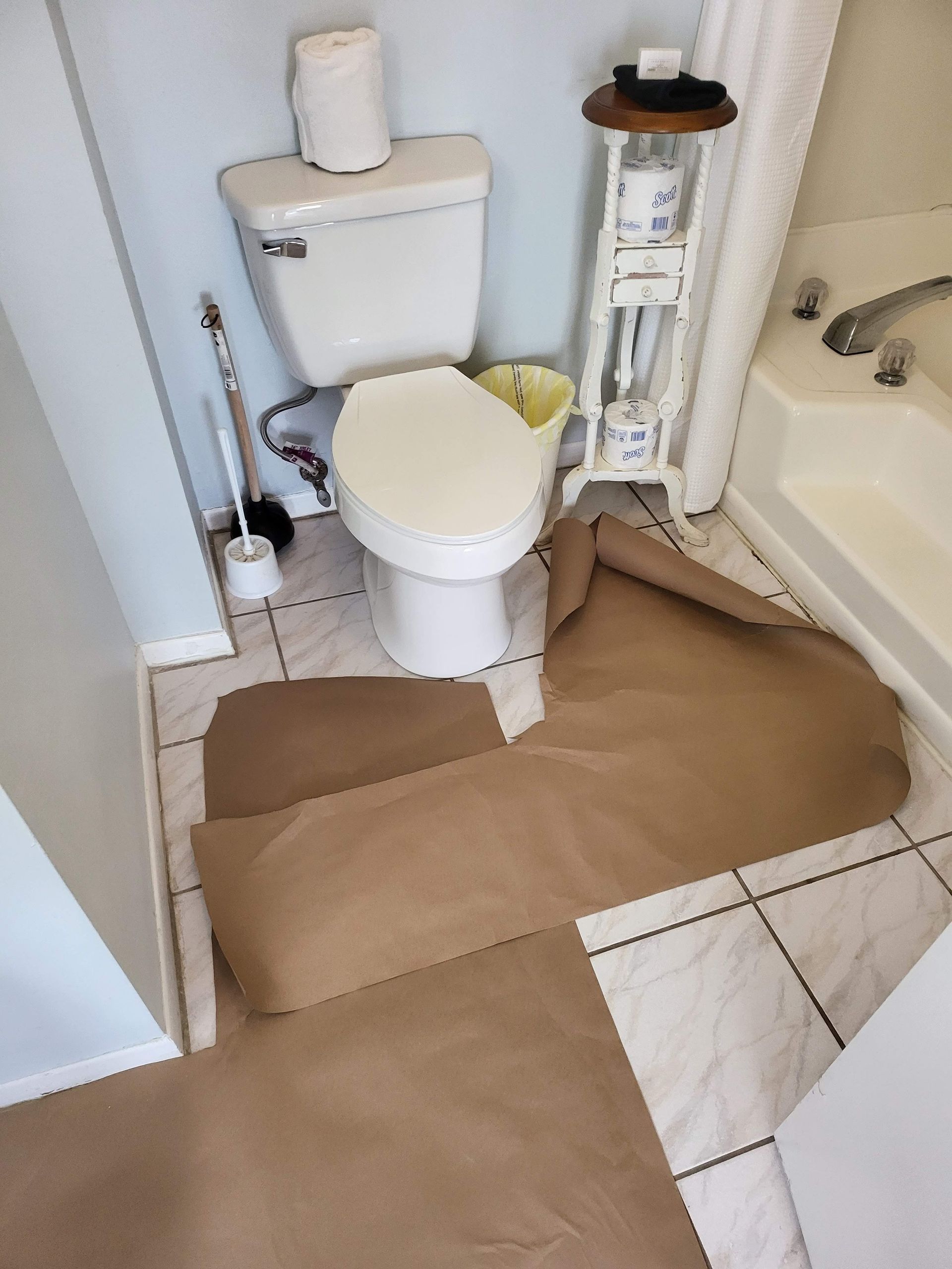 Bathroom with a toilet, shower, and brown protective floor covering extending into the doorway.