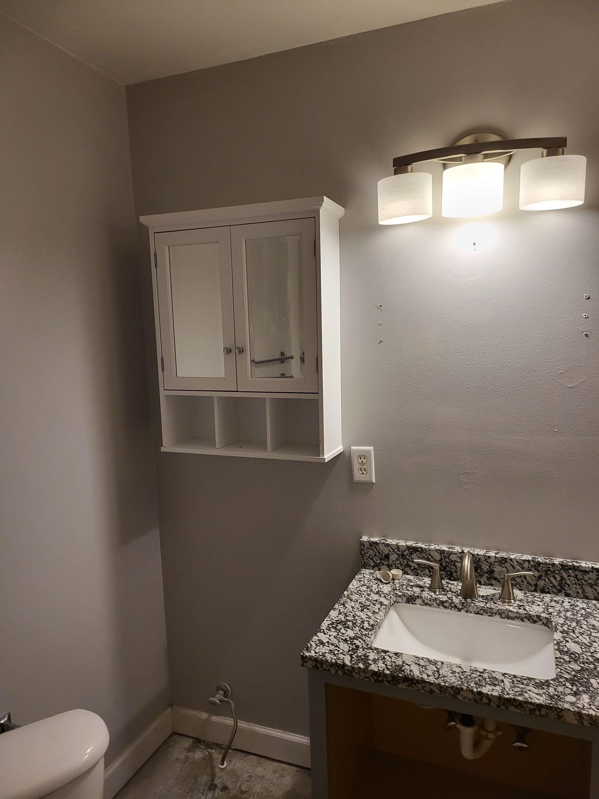 Small bathroom with gray walls, granite vanity, white sink, mirror cabinet, and wall light above.