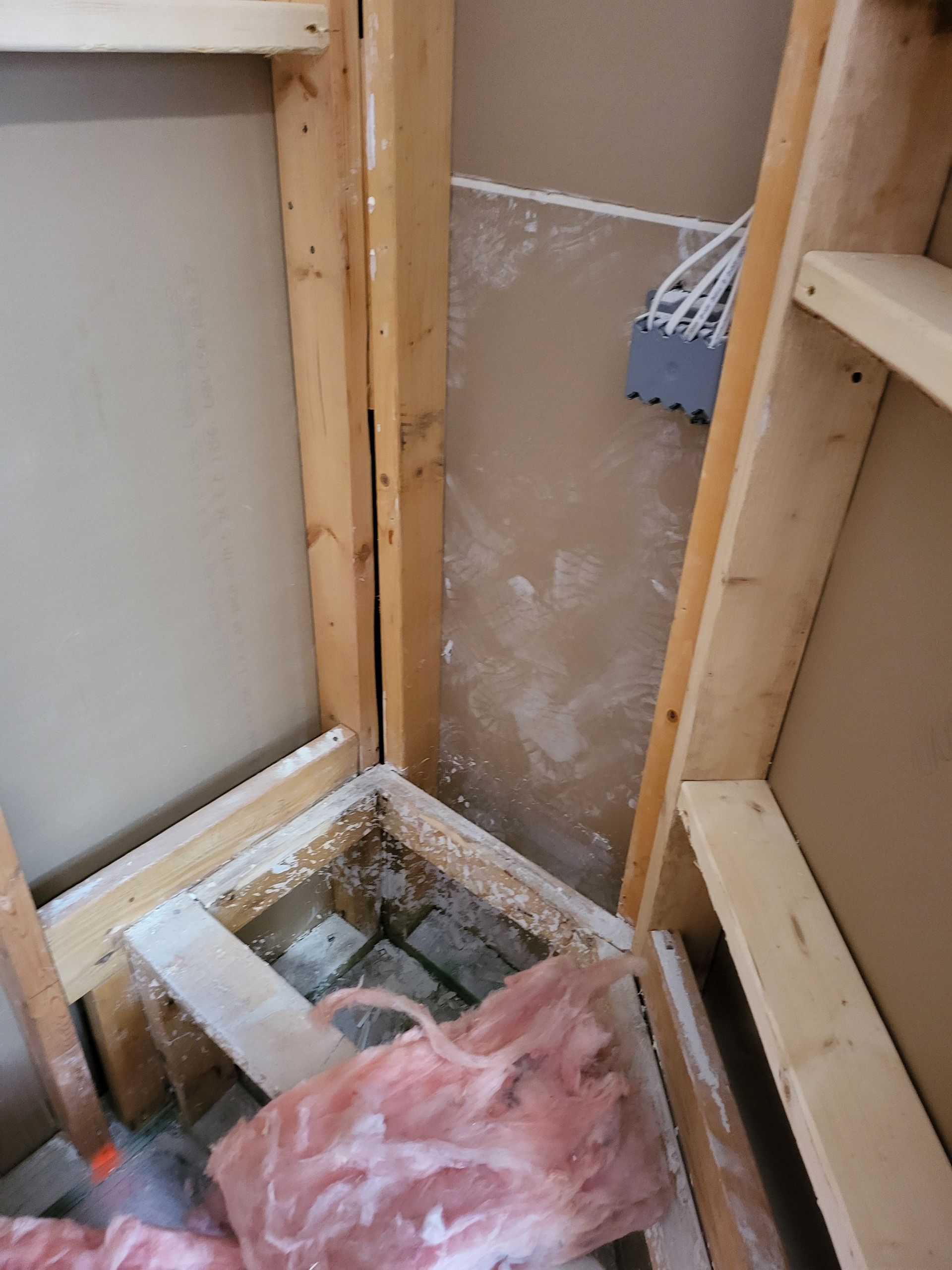 Partially built wall corner with exposed framing, debris, and pink insulation in a construction area