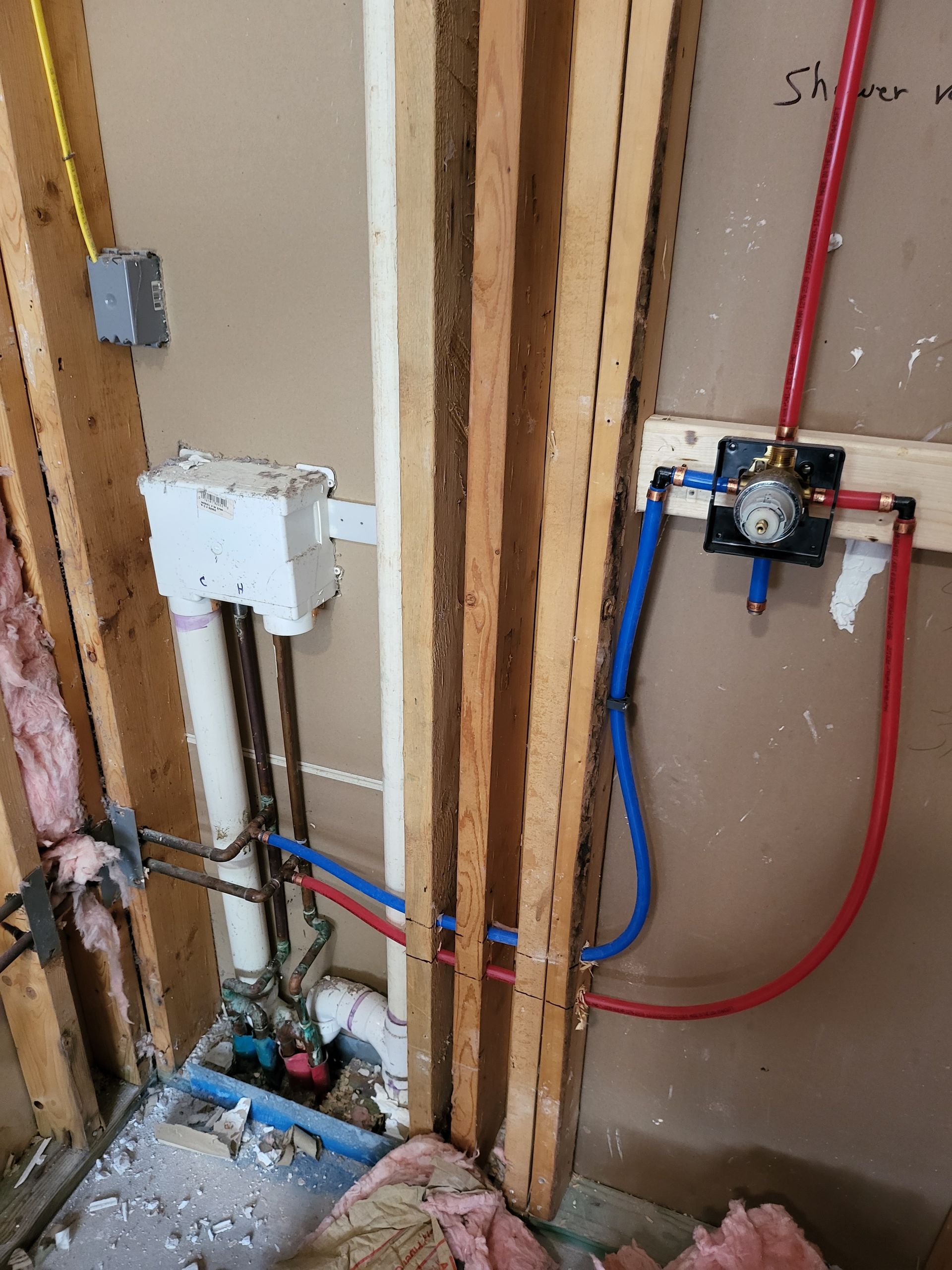 Exposed plumbing pipes and valves in an unfinished wall during bathroom renovation
