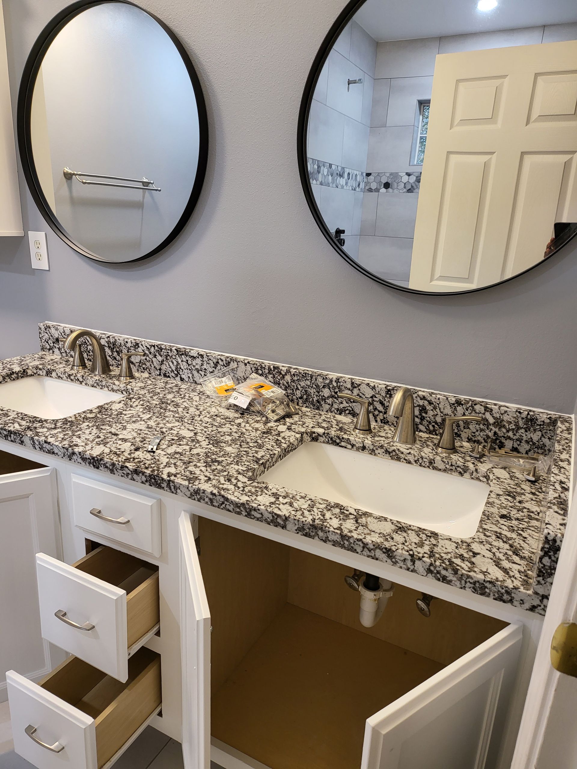 Bathroom vanity with granite countertop, double sinks, round mirrors, and one open cabinet and drawer