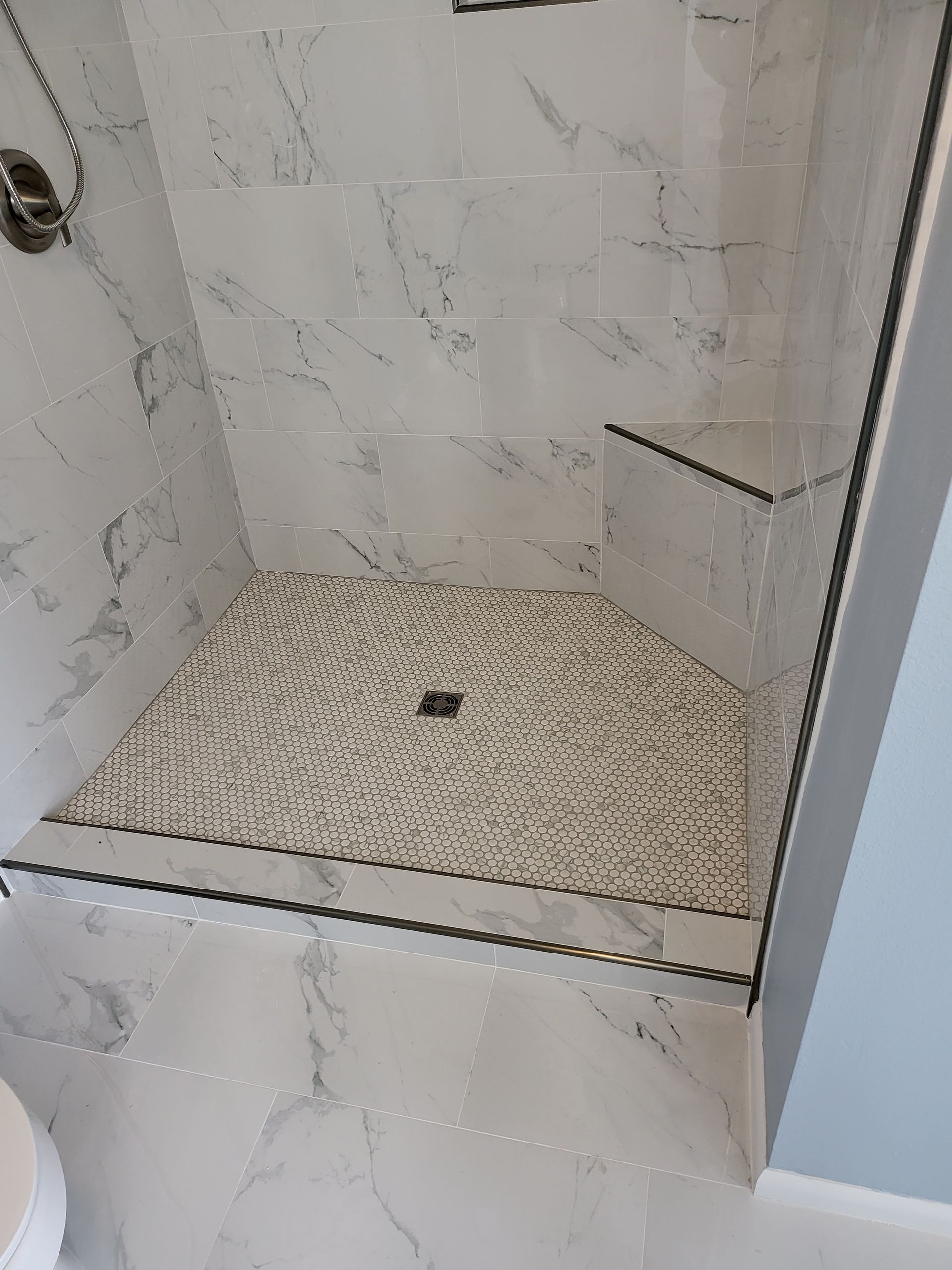Small tiled shower stall with white marble-look walls and pebble floor, no visible fixtures or glass door