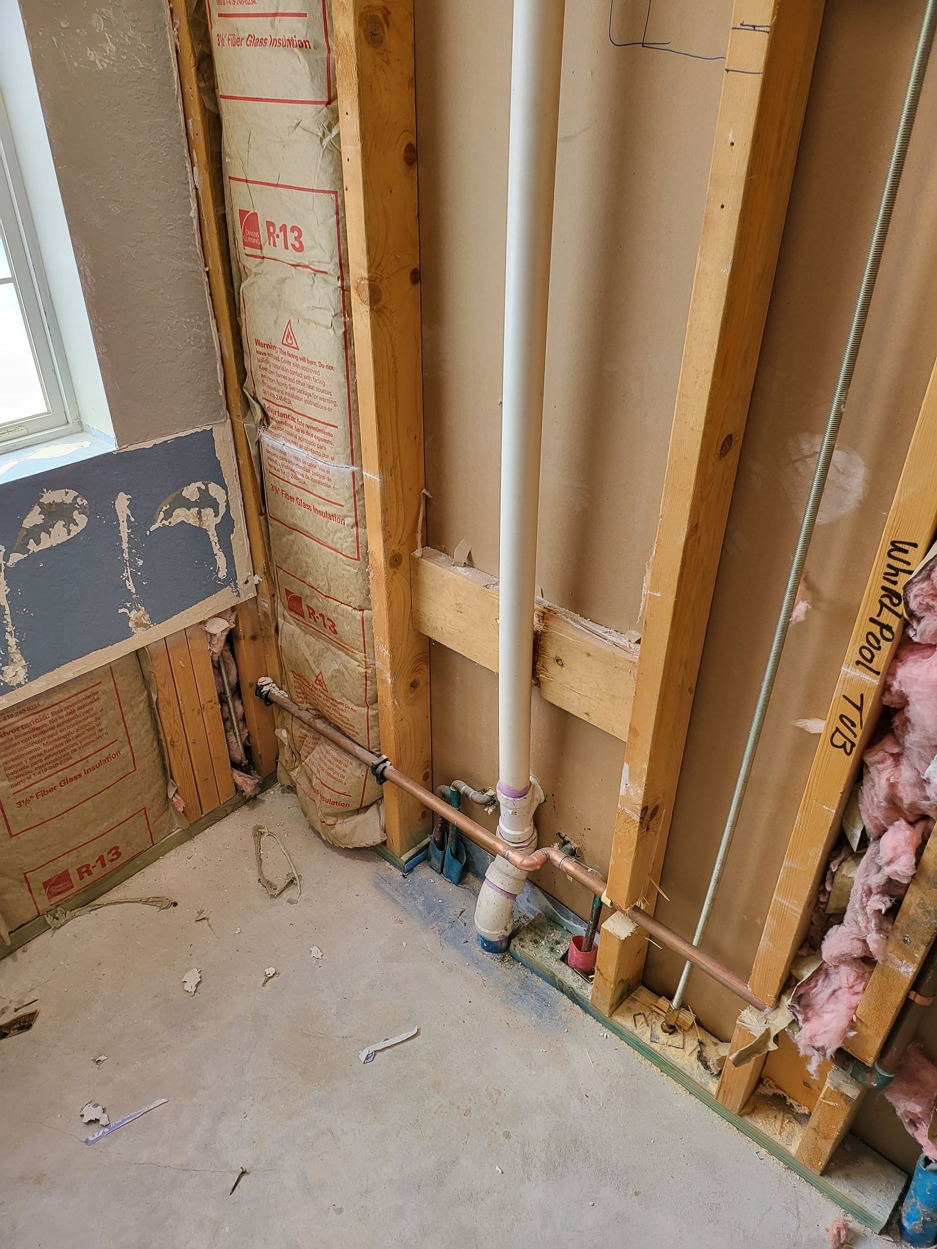 Partially framed wall with exposed studs, insulation, and plumbing in an unfinished room
