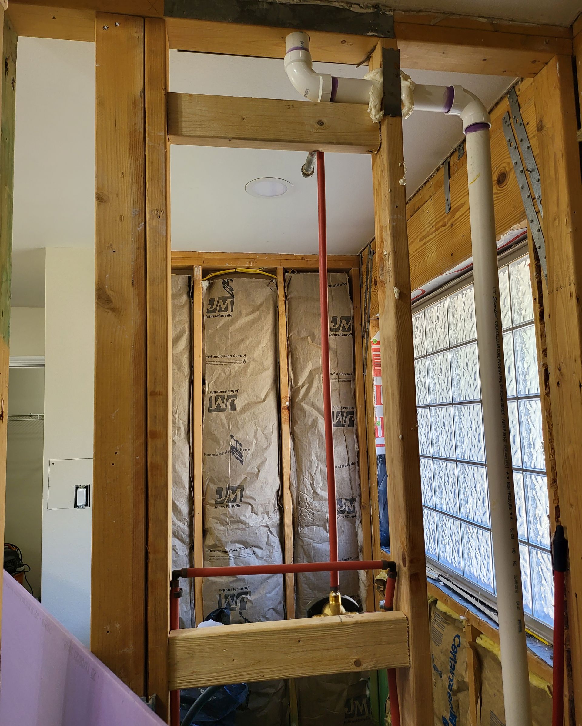 Partially renovated interior with exposed wooden framing, insulation, and red plumbing pipes.