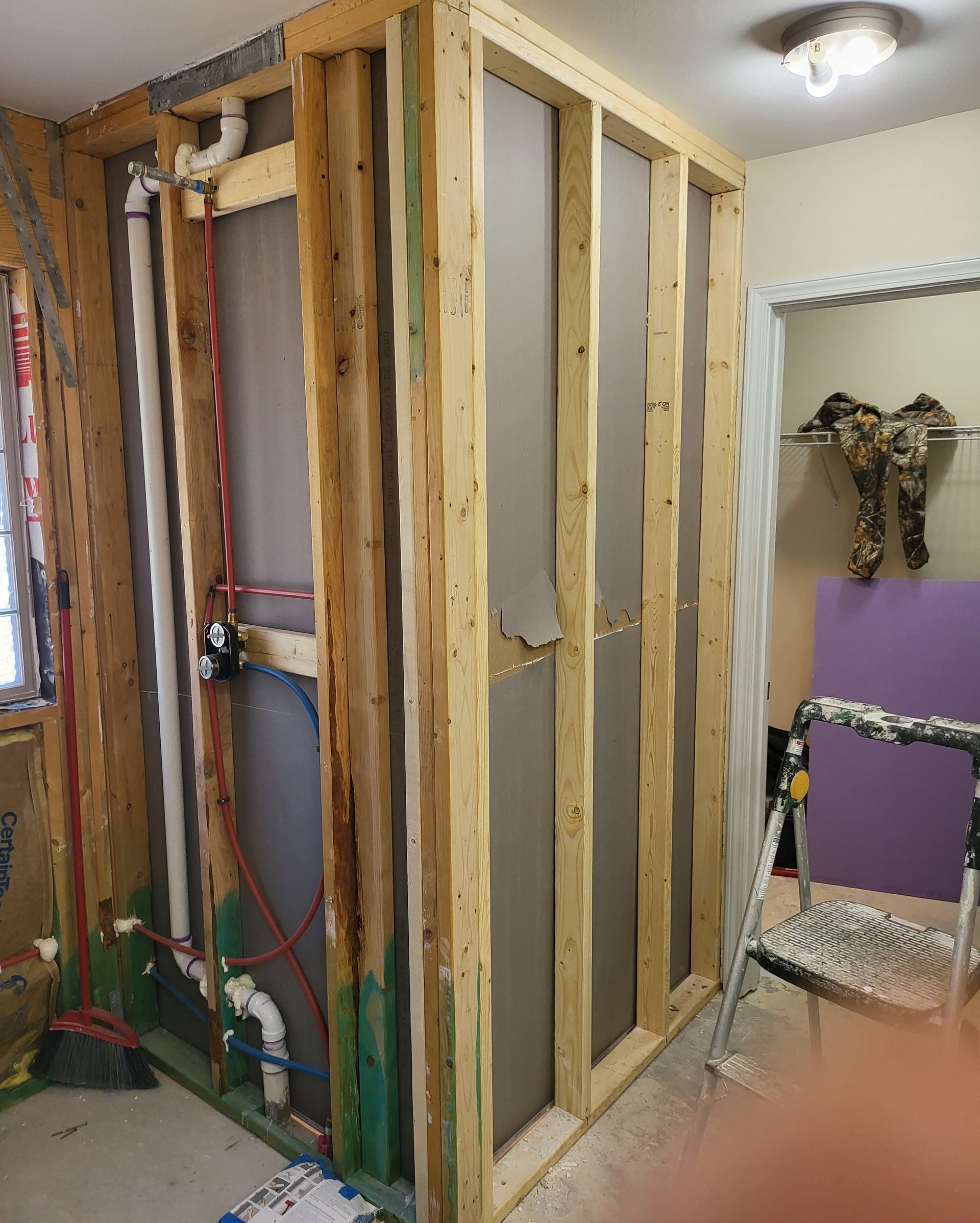 Framed interior wall under construction with exposed studs, insulation, and a doorway opening.