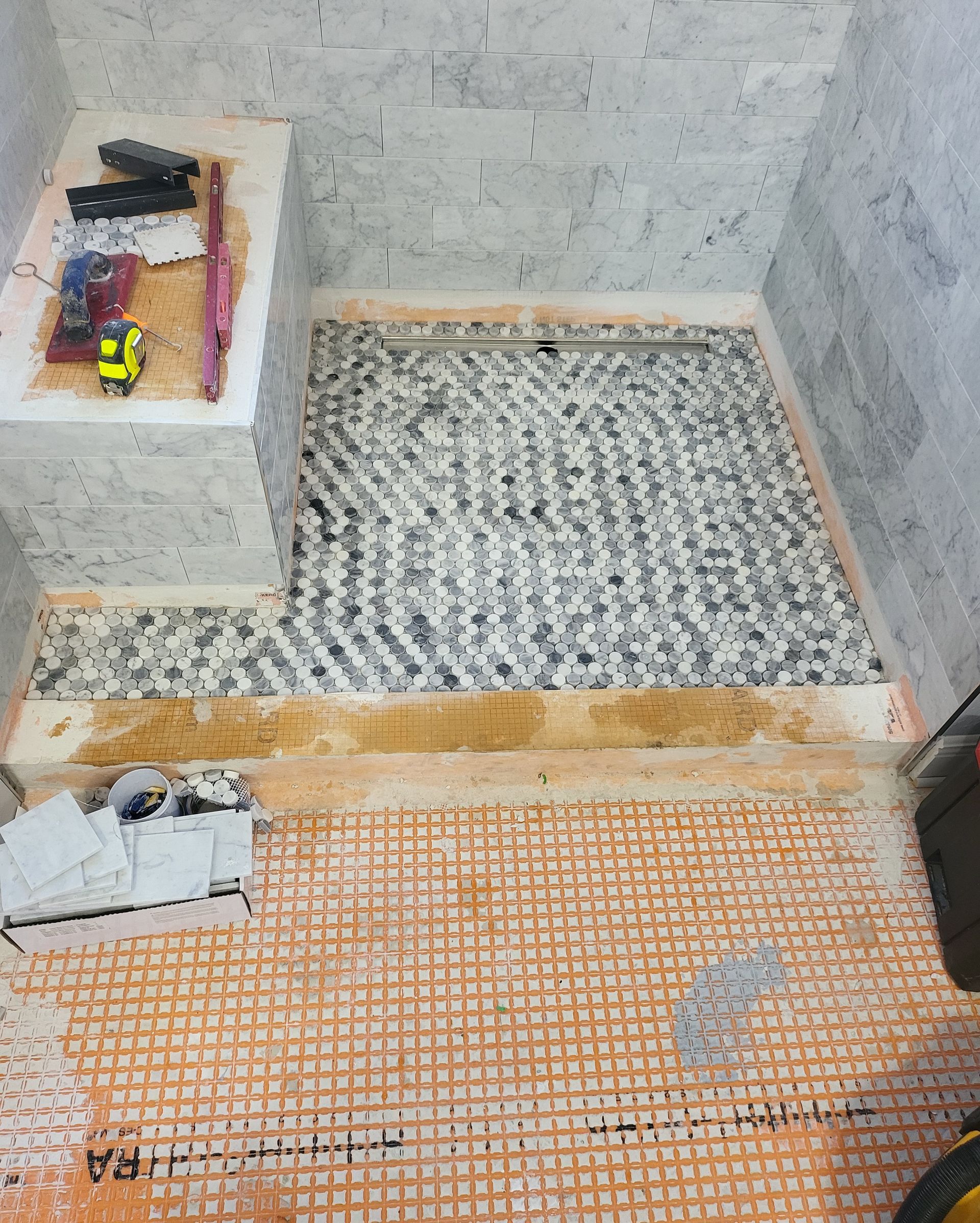 Small unfinished bathroom with tiled floor, concrete walls, a raised shower area, and a toilet base at left.
