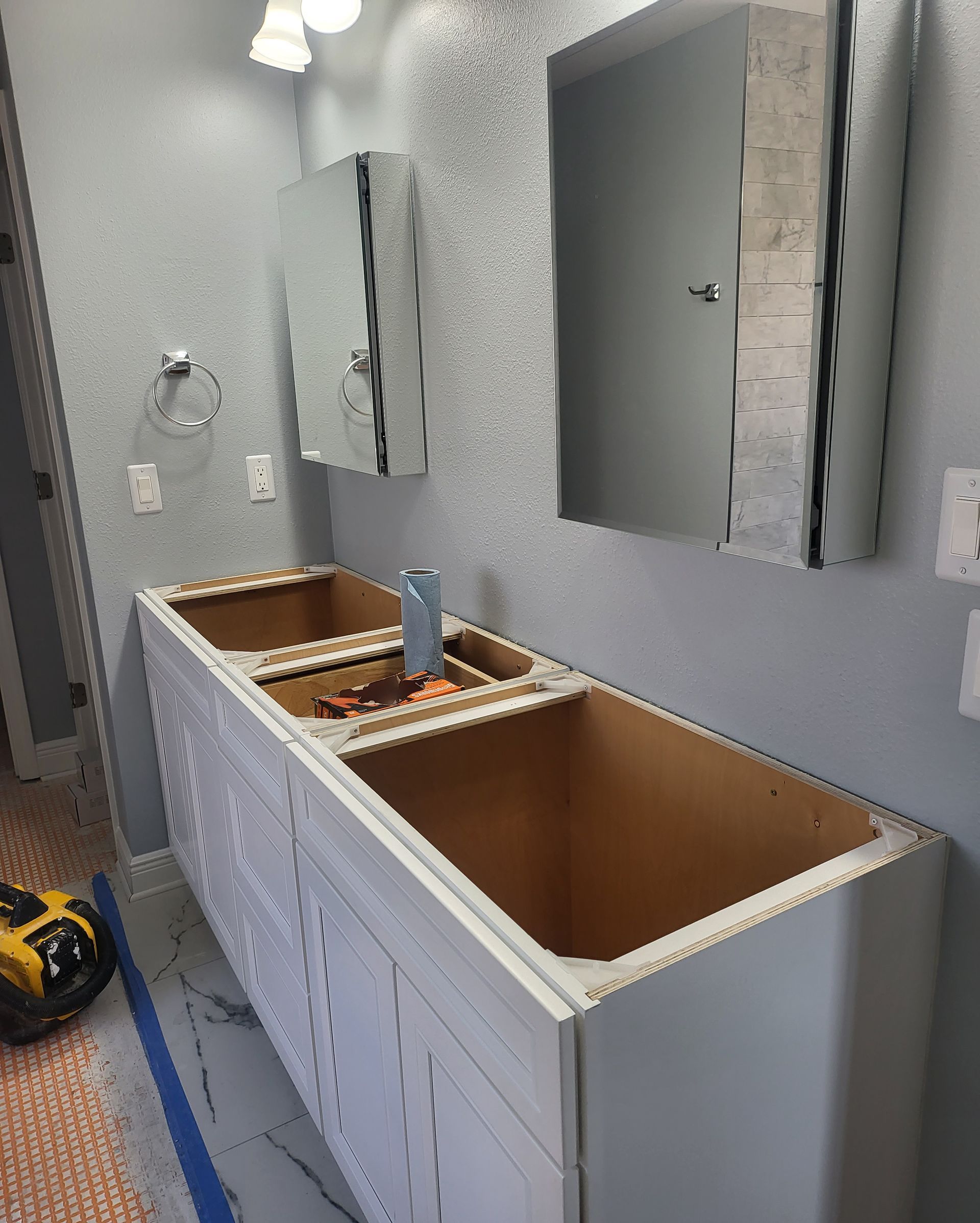 Bathroom vanity under renovation with two open sinks, gray walls, and mirrors above.