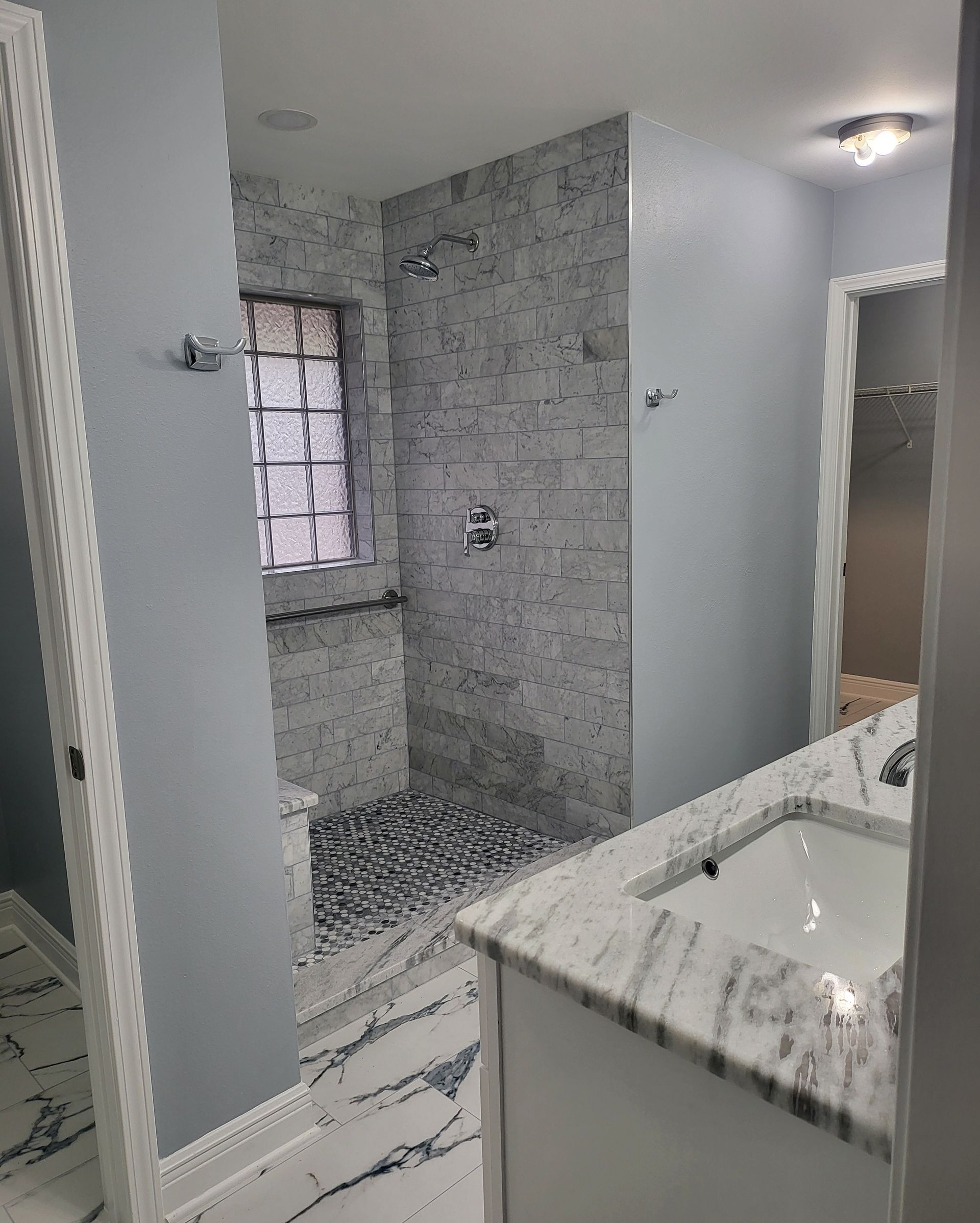 Modern bathroom with marble vanity, tiled shower, gray walls, and a window