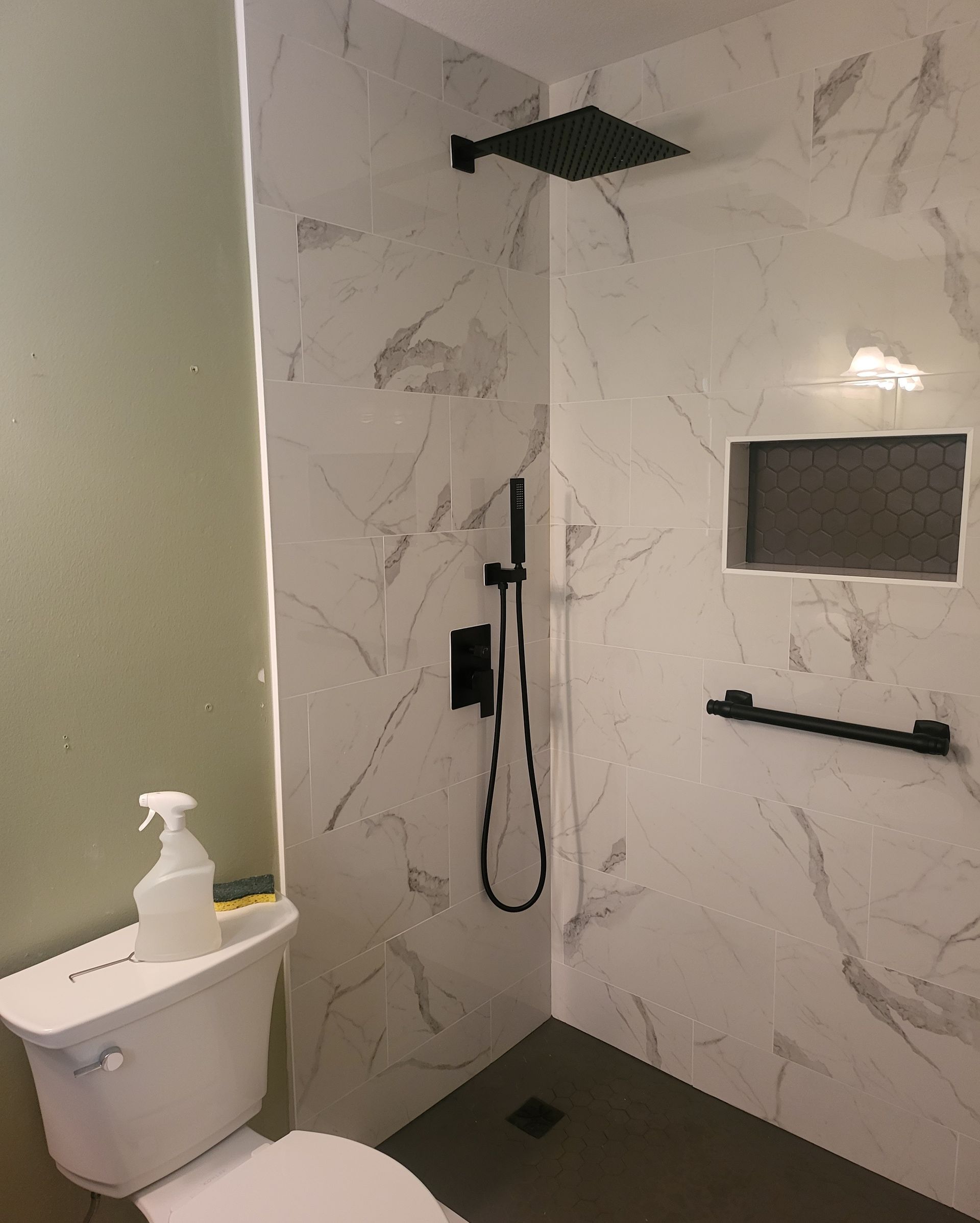 Modern shower room with white marble-look walls, black fixtures, toilet, and wall-mounted sink with soap dispenser