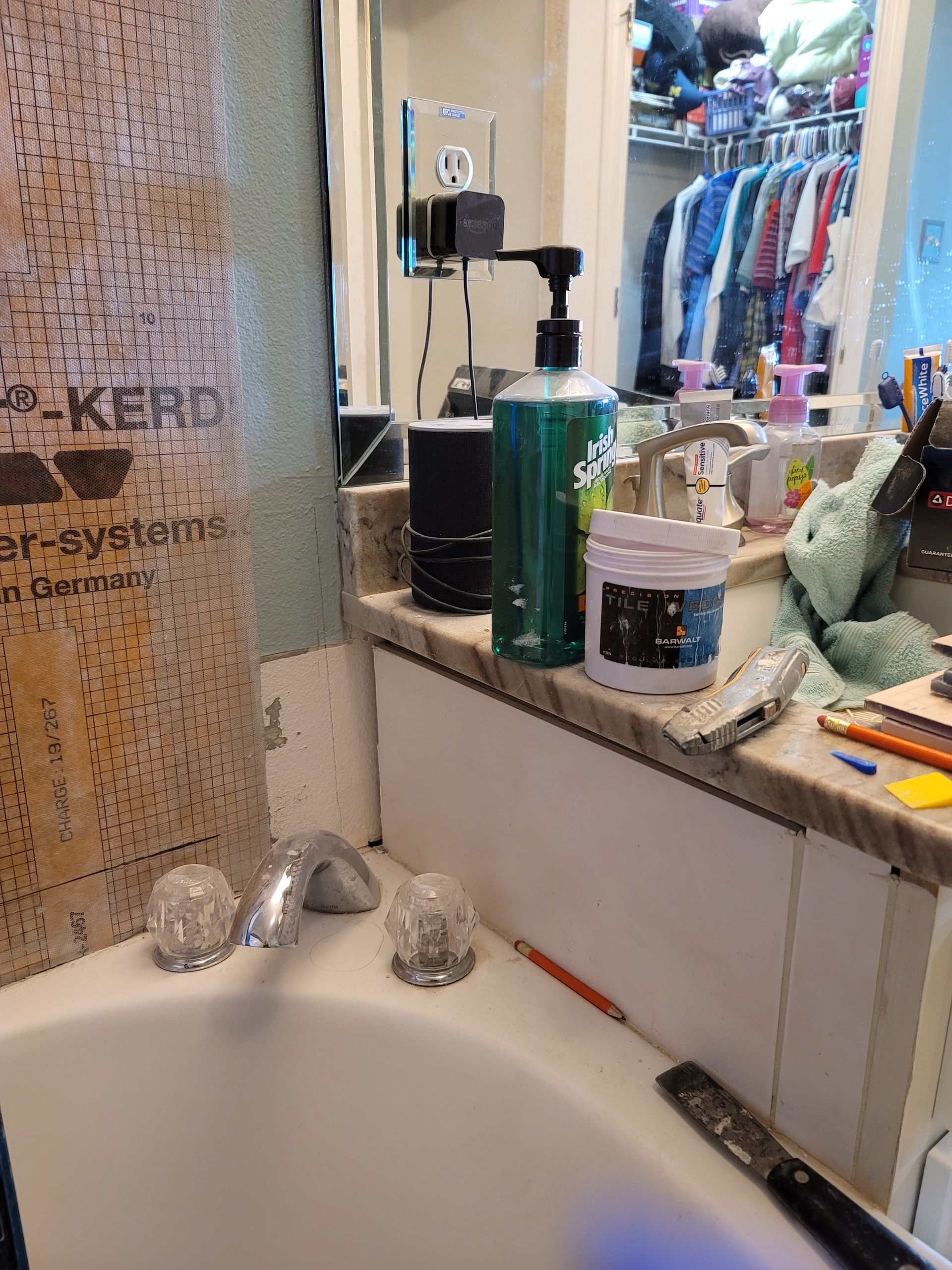 Bathroom sink with toiletries on the counter and a beige shower curtain beside a mirror.