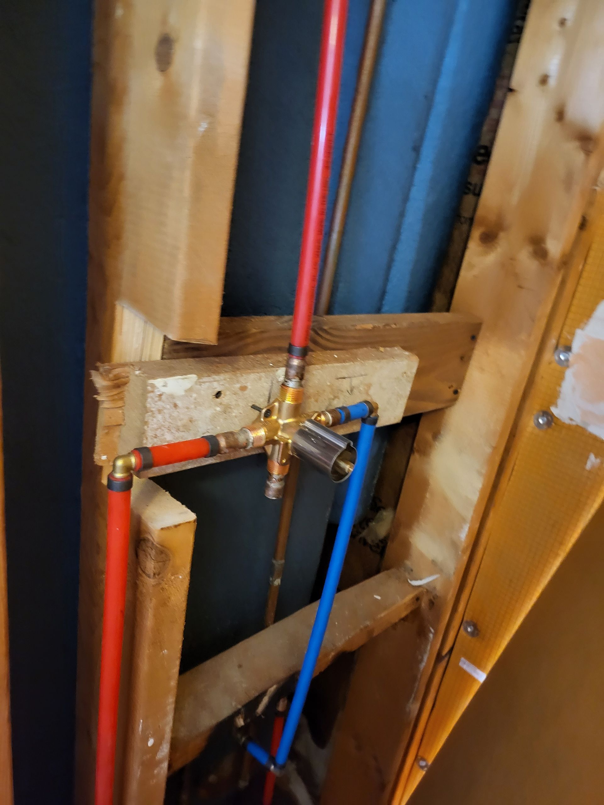 Plumbing pipes with red and blue water lines connected to a brass valve in a wall cavity
