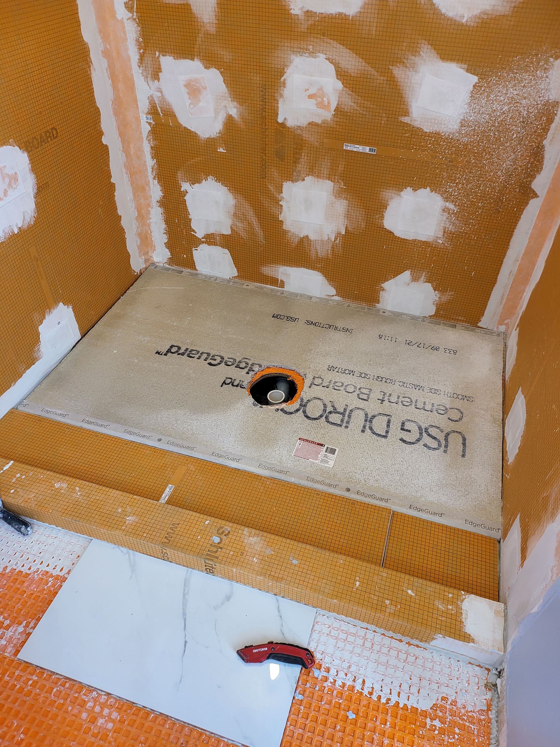 Orange plywood niche with white patchwork, a central cutout, and a red utility knife on the floor panel.