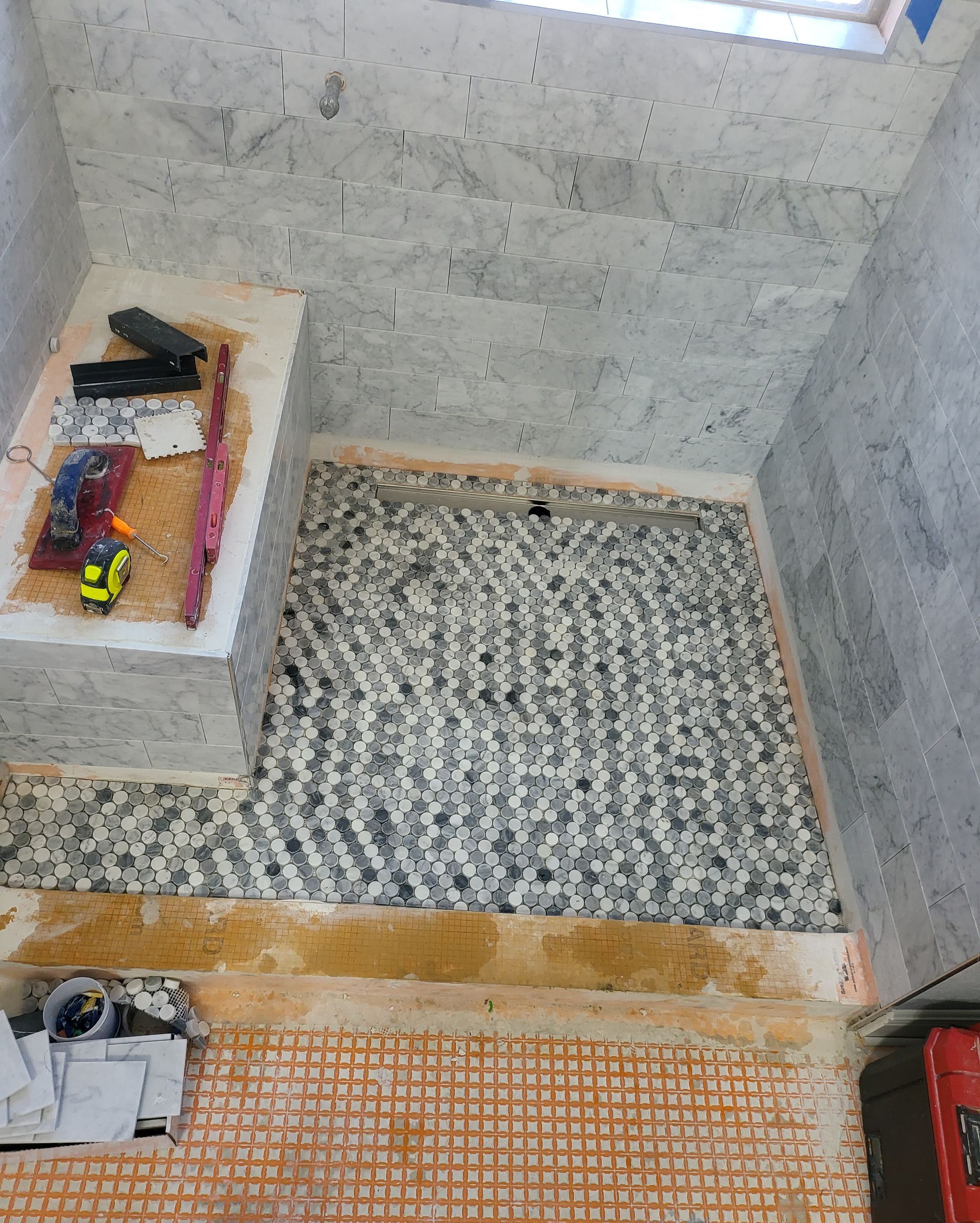 Small unfinished room with gray walls, a patterned floor mat, and a raised ledge holding tools and supplies.