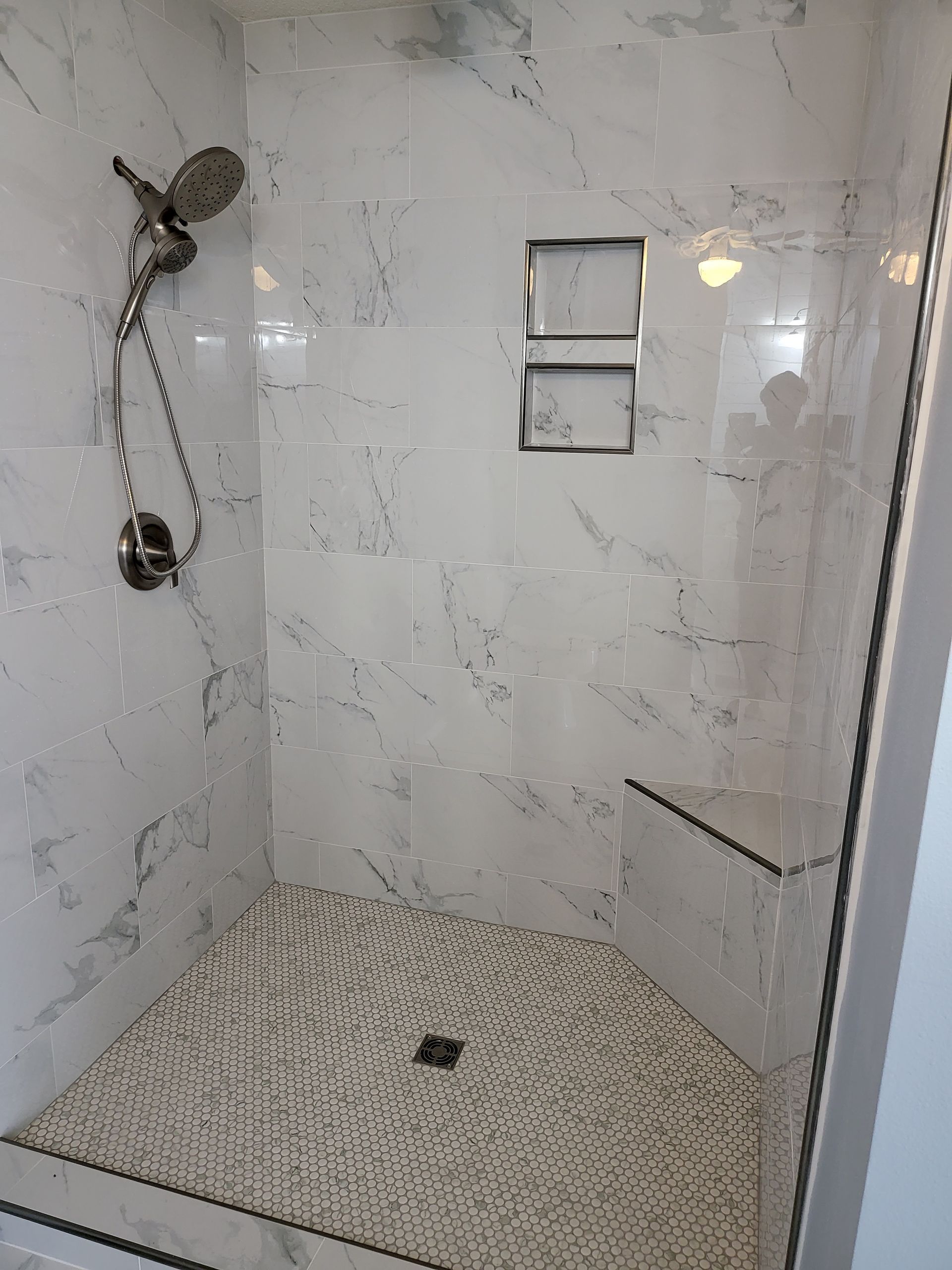 Empty tiled shower with mosaic floor, chrome showerhead, and two recessed wall niches.