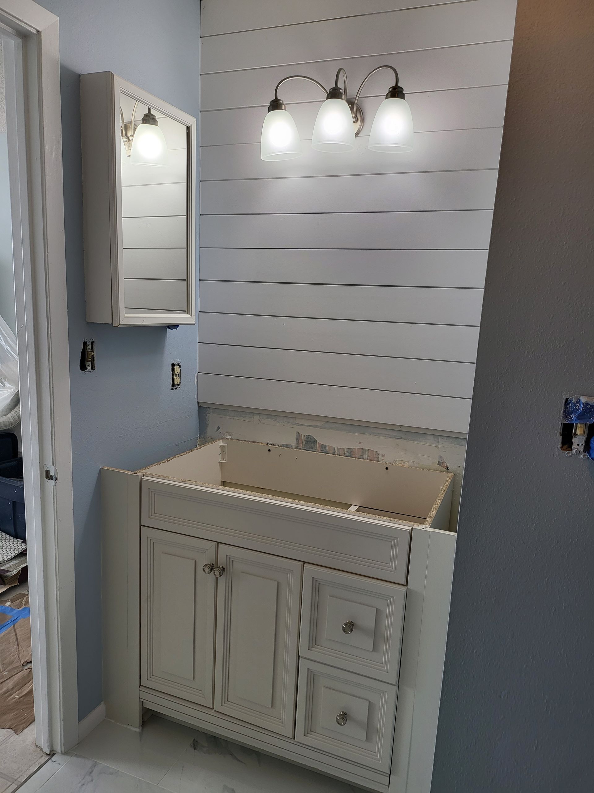 White bathroom vanity with sink, mirror cabinet, and three-light fixture against a slat wall.