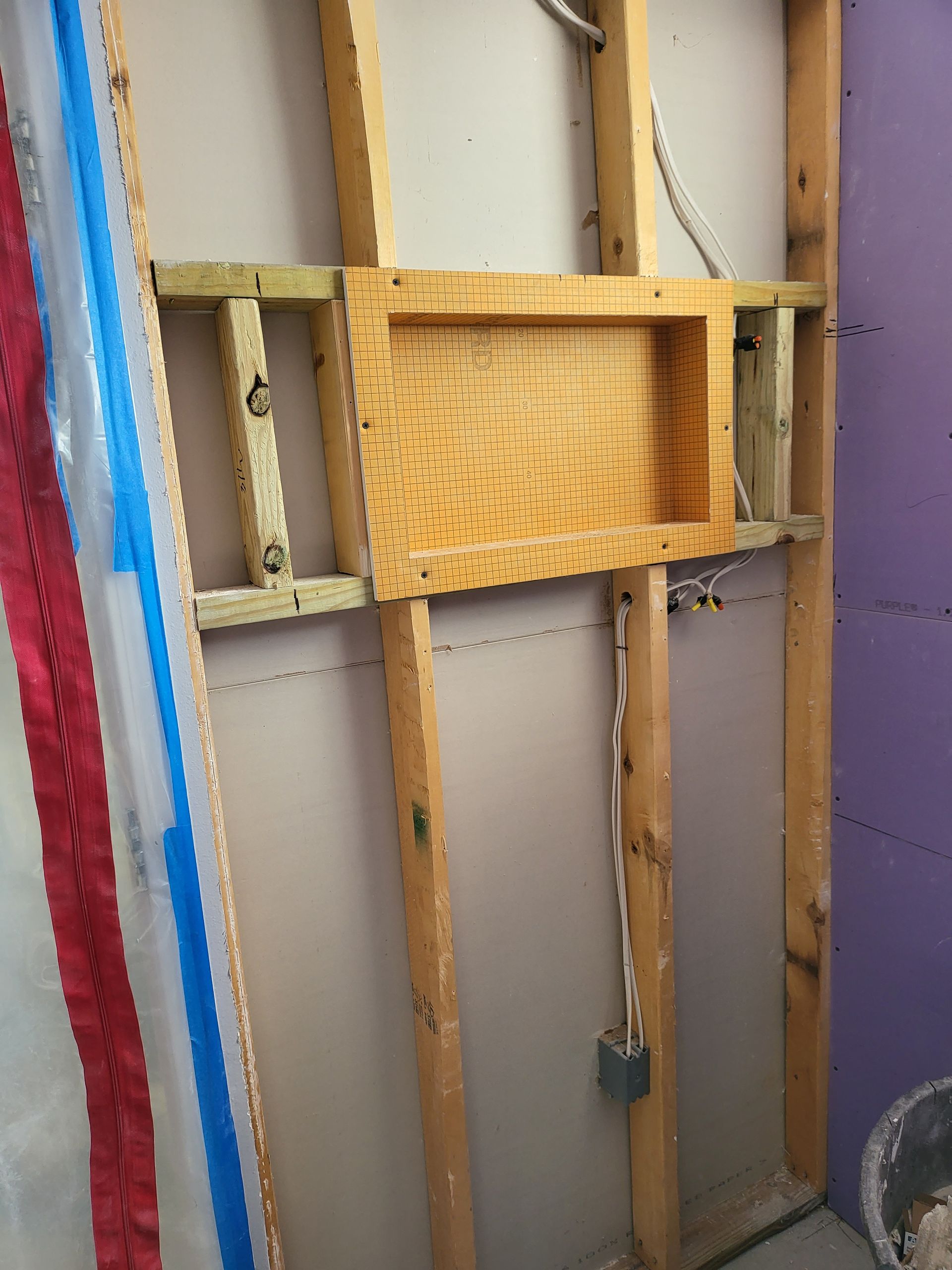 Exposed wall framing with a small woven wood shelf or panel and a blue-red painted strip on the left side.